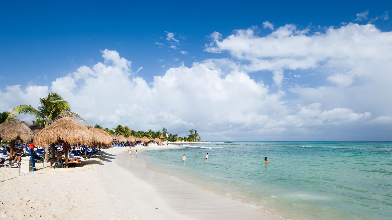 Cancun beach with palapa umbrellas, loungers, and swimmers in clear turquoise water under a bright blue sky. Cancun beach with palapa umbrellas, loungers, and swimmers in clear turquoise water under a bright blue sky.