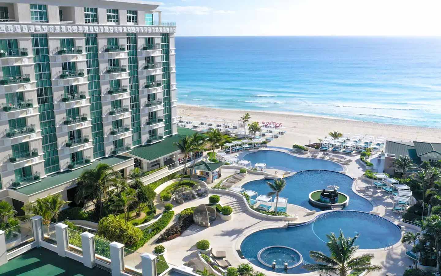 View of Sandos Cancun resort with tiered pools, cabanas, and beachfront loungers overlooking the turquoise Caribbean Sea.