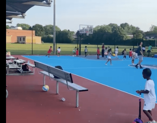 Four diverse young basketball players executing transition drills during small-group training session with coach supervising on gymnasium court