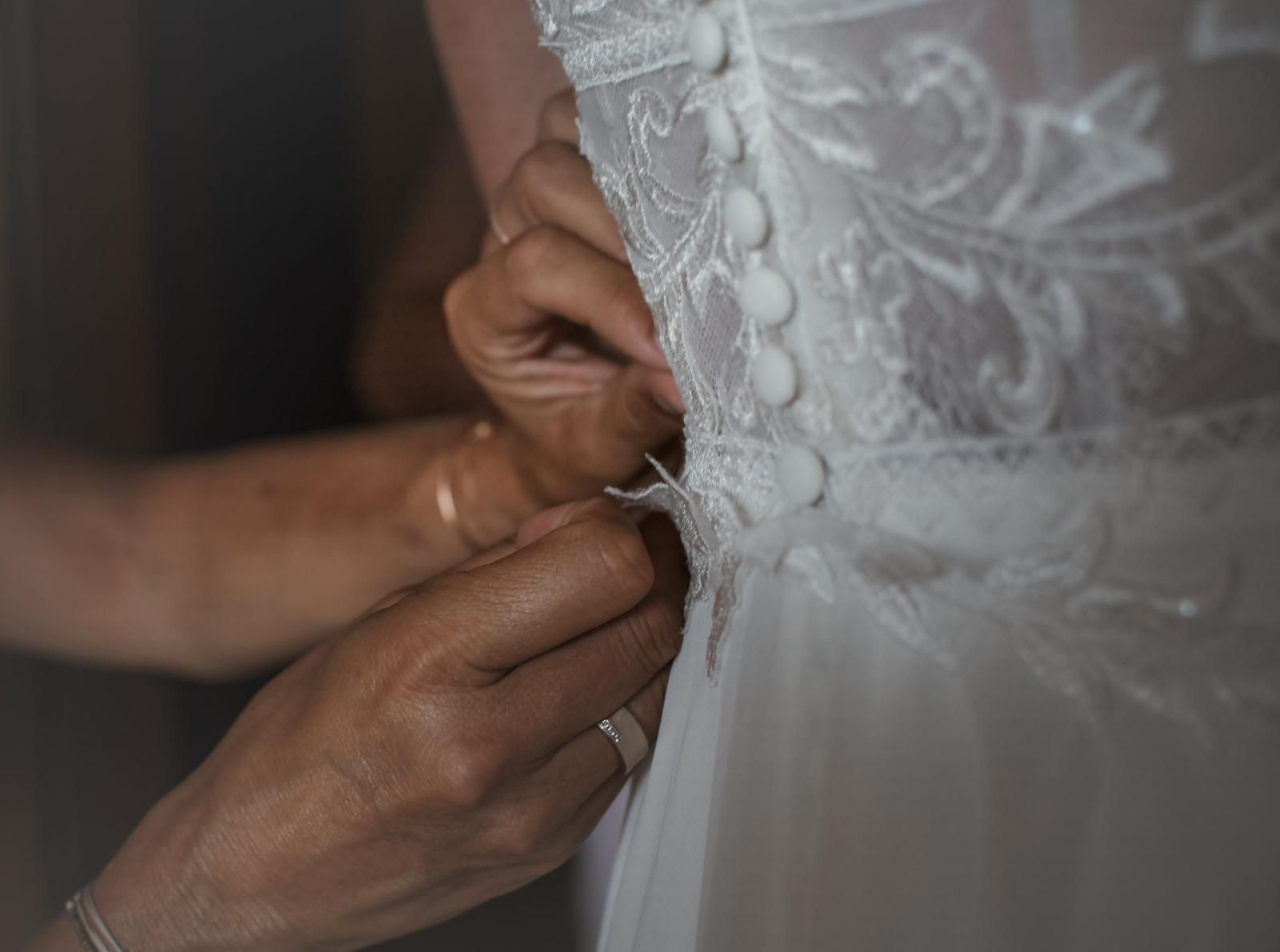 Hände schließen die Knöpfe eines Brautkleides während des Getting Ready Hände schließen die Knöpfe eines Brautkleides während des Getting Ready