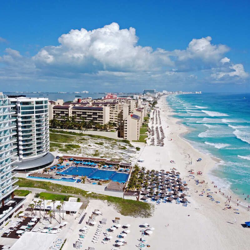 Aerial view of Cancun's white-sand beach lined with luxury resorts, turquoise Caribbean waters, beachfront pools, and upscale accommodations showcasing the destination's evolution into a sophisticated luxury travel hotspot.