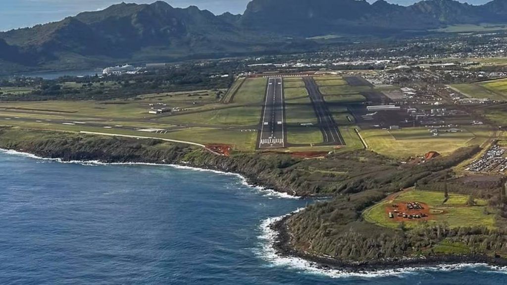 Aerial view of Līhuʻe Airport on the island of Kauai, Hawaii, with its runway stretching along the Pacific coastline and lush green mountains rising in the background. Aerial view of Līhuʻe Airport on the island of Kauai, Hawaii, with its runway stretching along the Pacific coastline and lush green mountains rising in the background.