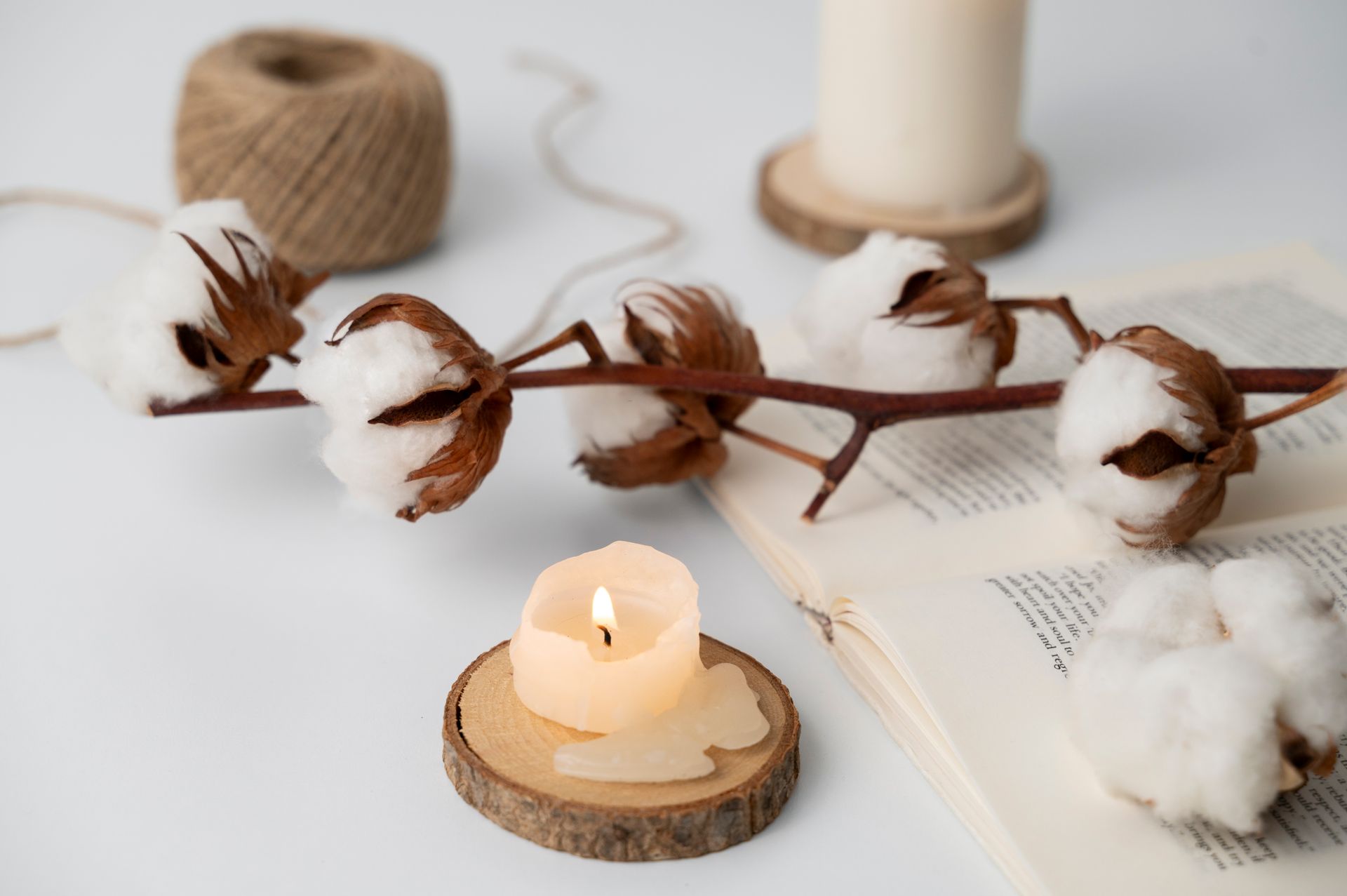 bougie qui ce consume sur un morceau de bois, esprit cocooning avec une branche de fleur de coton, un livre ouvert sur une table blanche. bougie qui ce consume sur un morceau de bois, esprit cocooning avec une branche de fleur de coton, un livre ouvert sur une table blanche.
