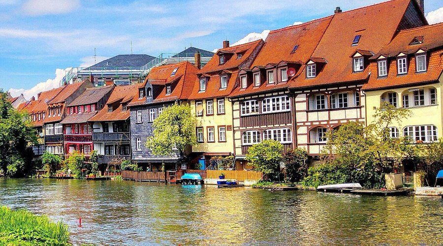 Colorful half-timbered homes lining the river in Bamberg Altstadt, Germany, with reflections shimmering on the water beneath a sunny sky.