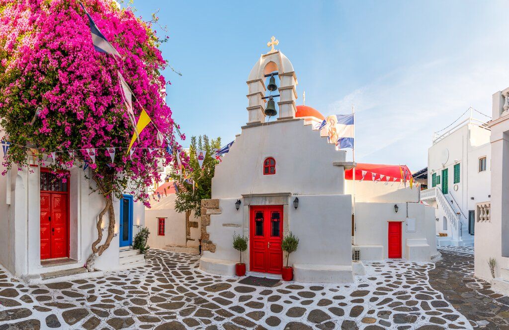 Whitewashed Mykonos church with red doors and bougainvillea.