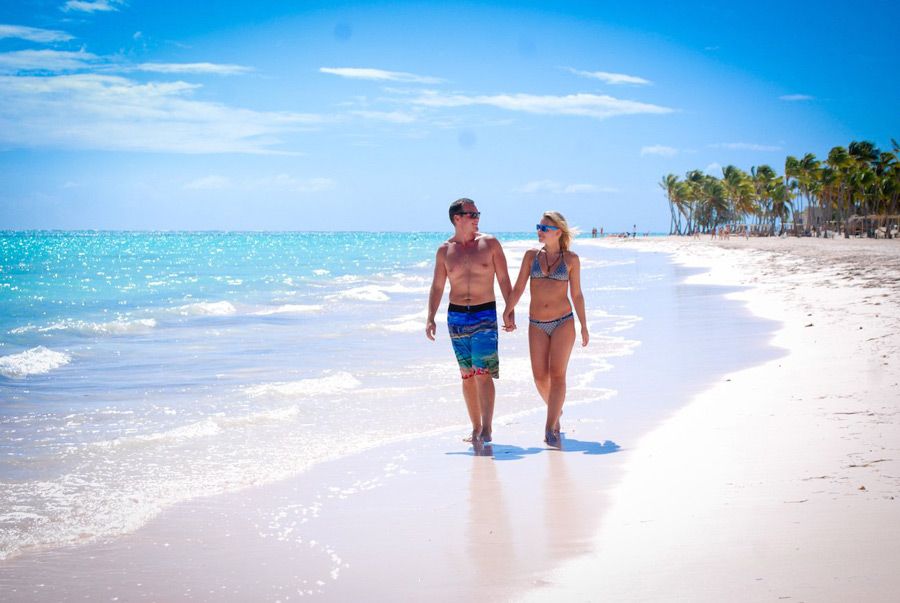 A couple walking hand-in-hand along a white-sand beach in Punta Cana, with turquoise water, palm trees, and clear skies in the background. A couple walking hand-in-hand along a white-sand beach in Punta Cana, with turquoise water, palm trees, and clear skies in the background.