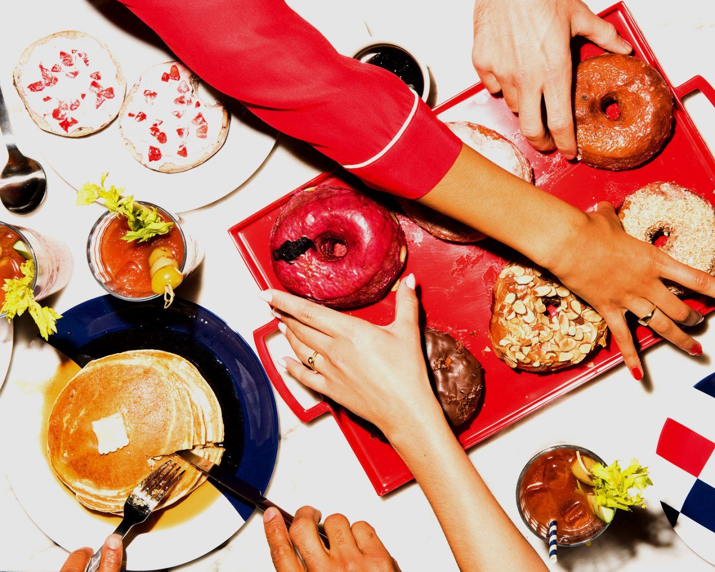 Hands reaching for gourmet donuts and brunch plates with cocktails on a table