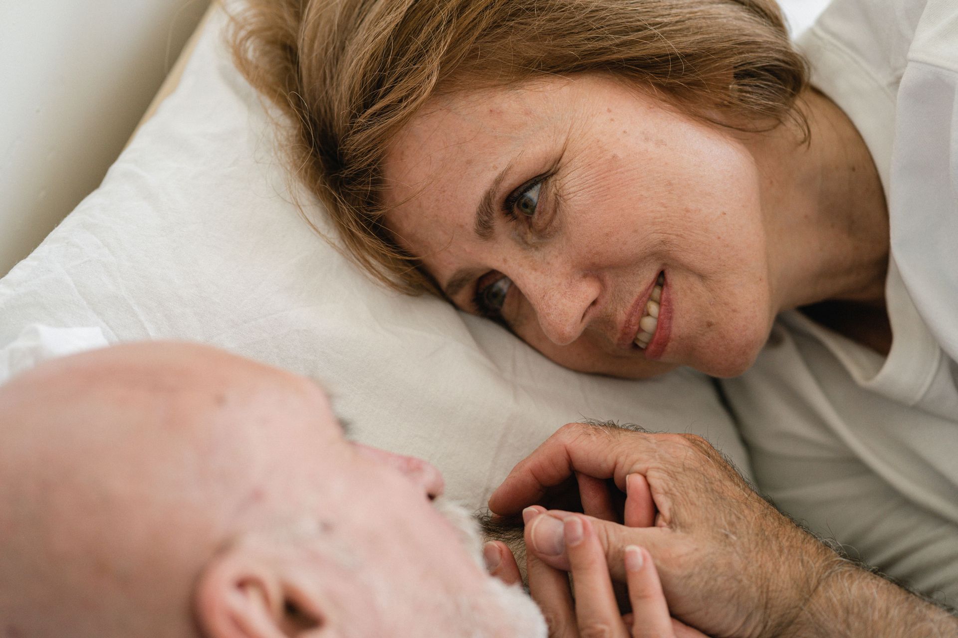 Close up of a mature woman holding the hand of an elderly man in bed