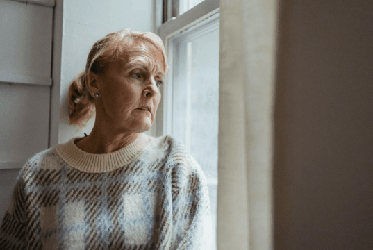 Older woman with worried face is looking out a window