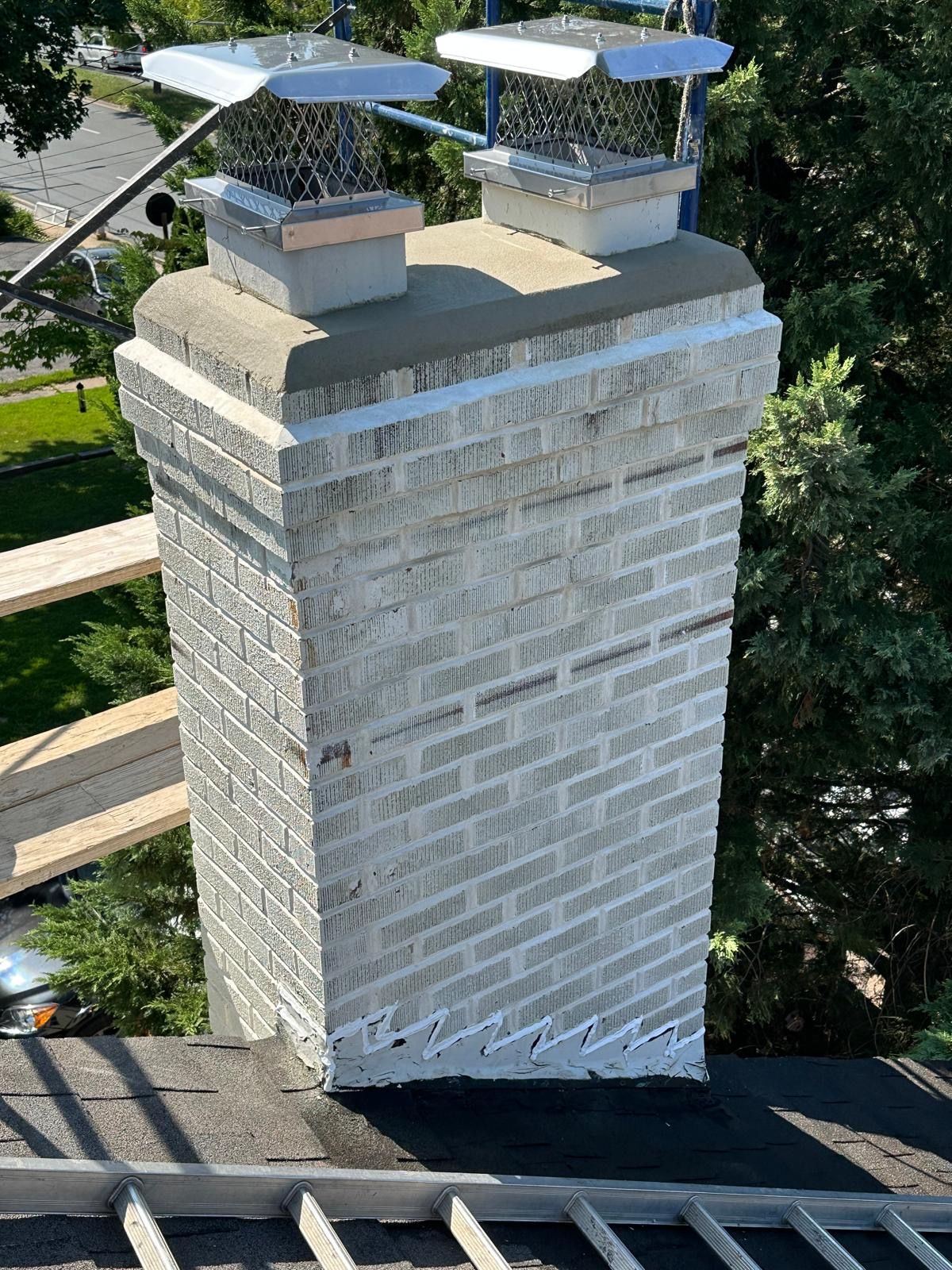 Technician inspecting chimney opening on residential roofline during afternoon light, with neighborhood visible below