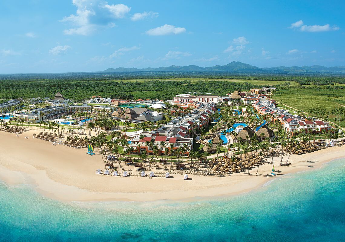 Aerial view of a luxury beachfront resort in Punta Cana with turquoise water, palm trees, and white sand beach stretching along the coast.