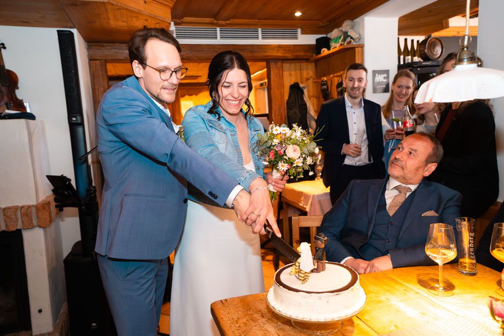 Tortenanschnitt bei Hochzeit mit Wunderkerzen und Gästen im Hintergrund
