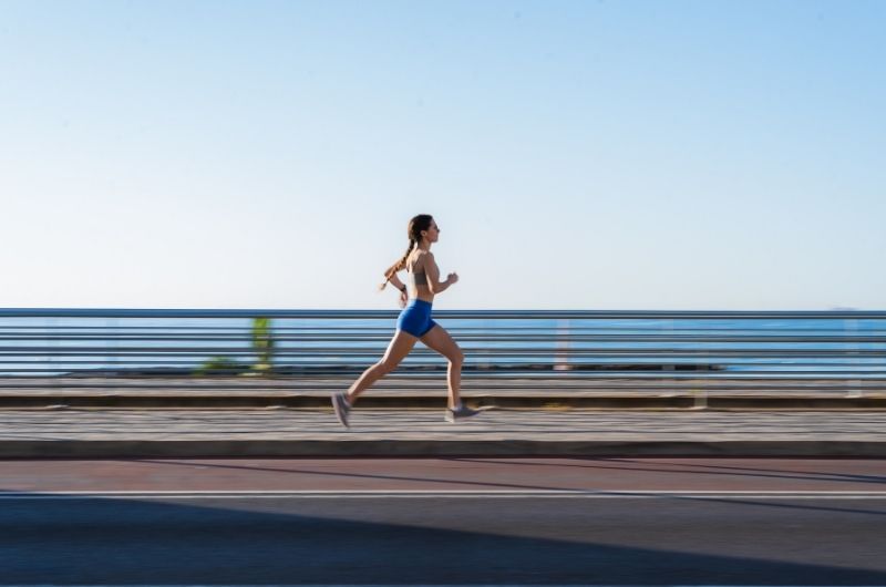 Person jogging on sunlit park path with trees, natural morning light during daily fitness activity