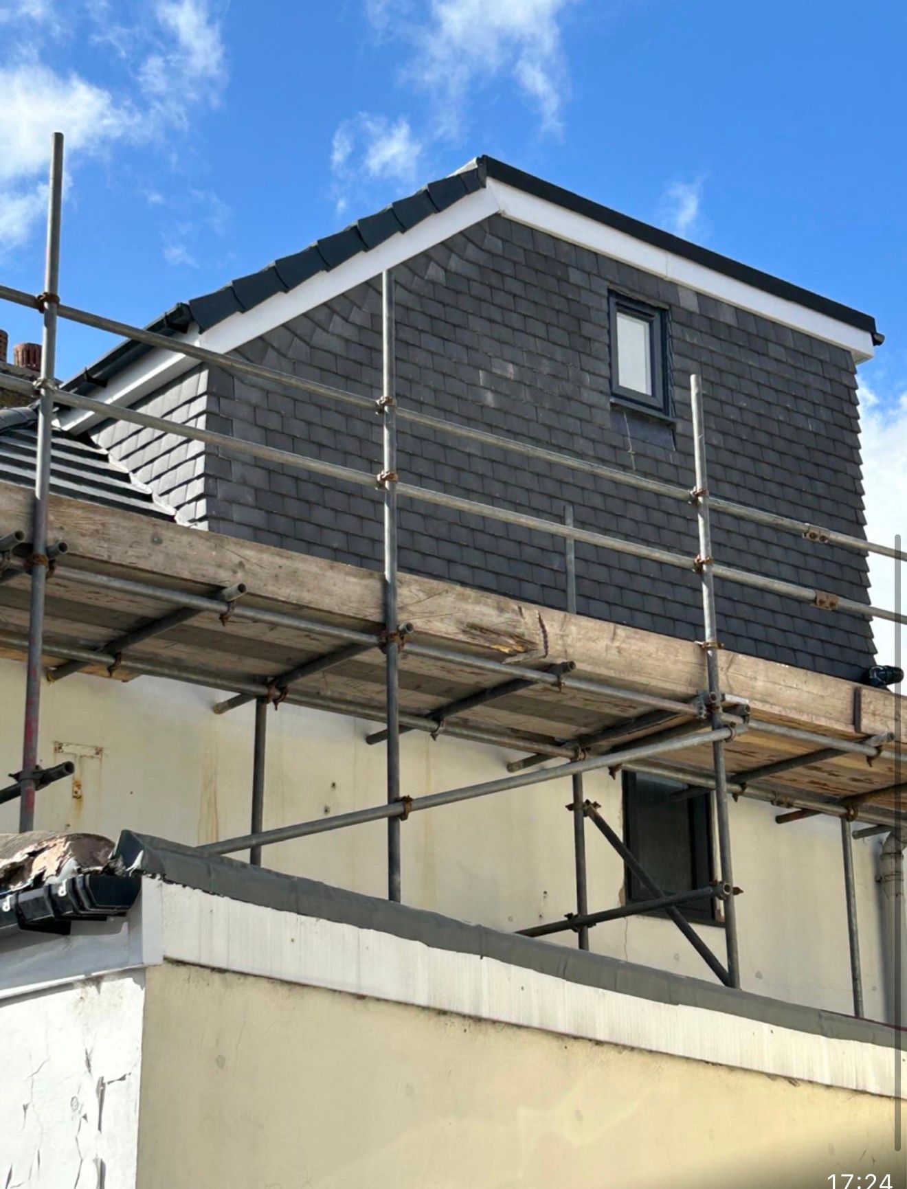Two skilled roofers installing slate tiles on pitched residential roof with visible safety equipment