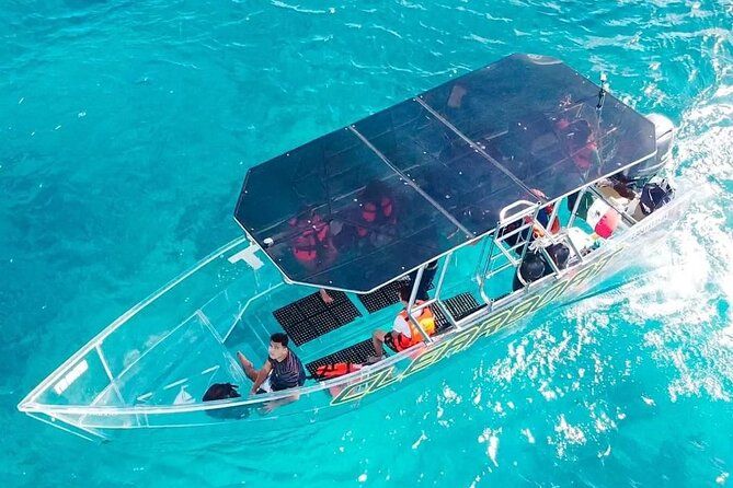 A clear-bottom tour boat floats on bright turquoise water with passengers seated under a canopy.
