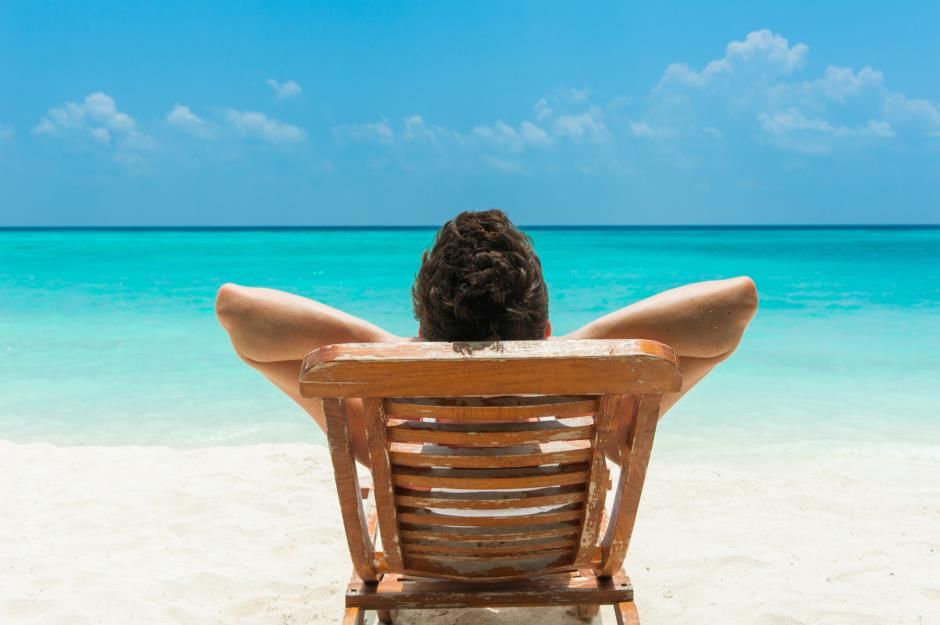 Person relaxing in a wooden beach chair facing turquoise ocean water under a sunny blue sky. Person relaxing in a wooden beach chair facing turquoise ocean water under a sunny blue sky.