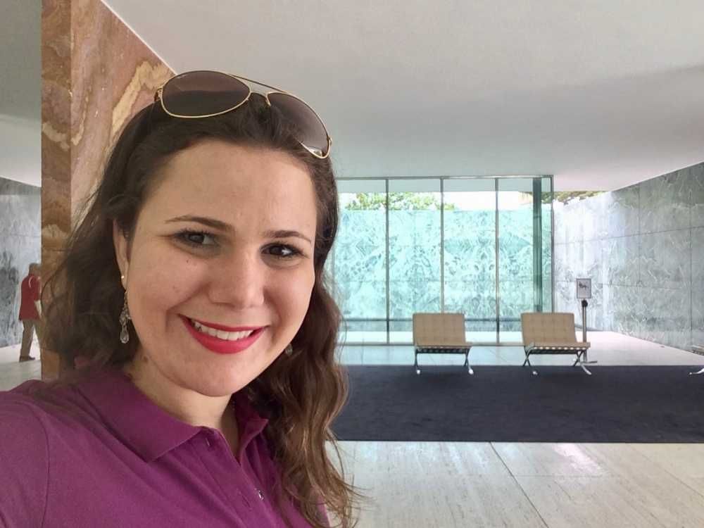 Foto da autora dentro do Pavilhão com as famosas cadeiras Barcelona ao fundo