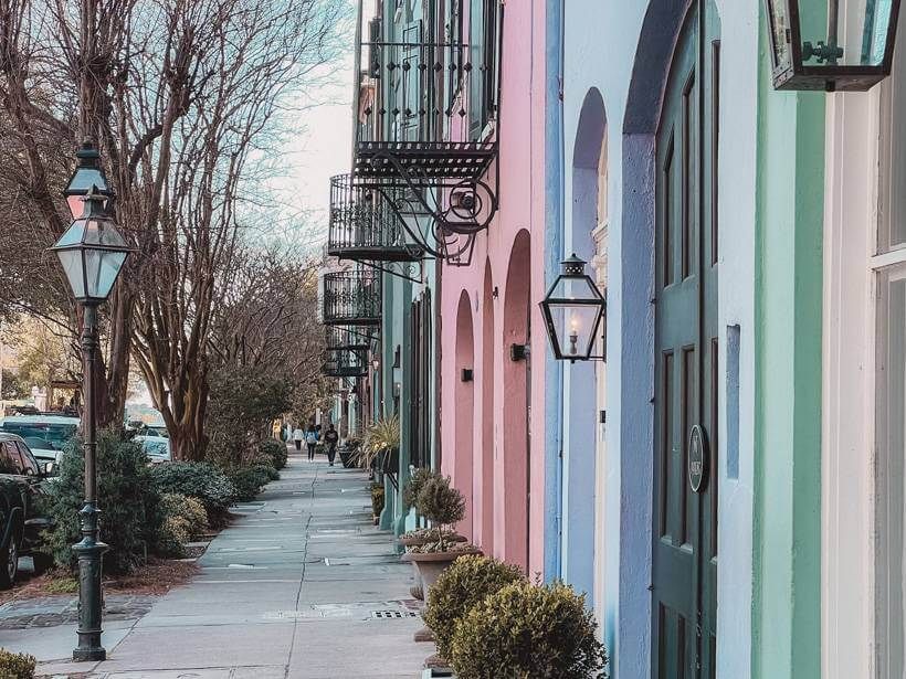 Pastel-colored historic homes along Rainbow Row in Charleston, SC, with lantern lights and a tree-lined sidewalk.