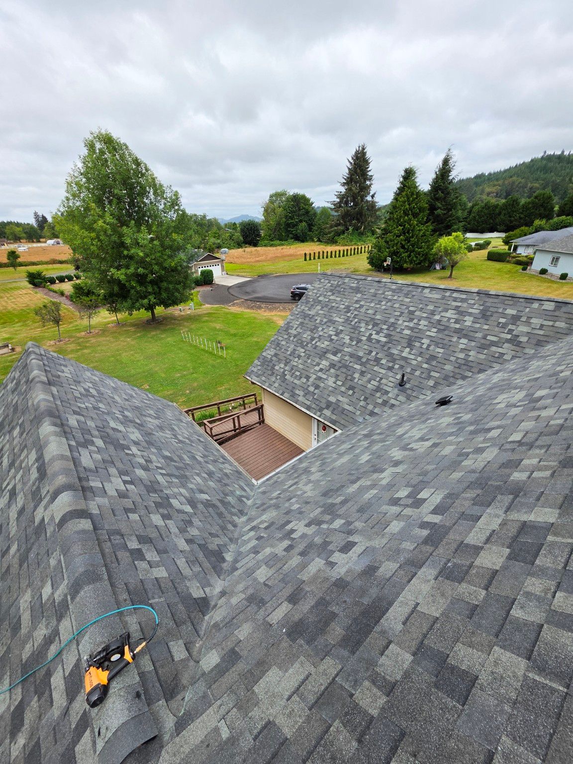 Architectural shingle roof with intersecting slopes and a central valley, overlooking a wood deck and tree-lined yard. Architectural shingle roof with intersecting slopes and a central valley, overlooking a wood deck and tree-lined yard.