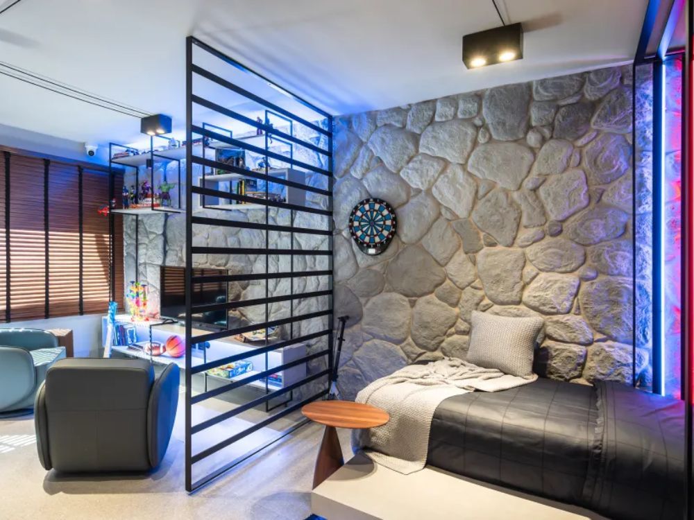 Quarto com parede de pedras, grades dividindo ambiente com um espaço de estar e iluminação em tons de azul