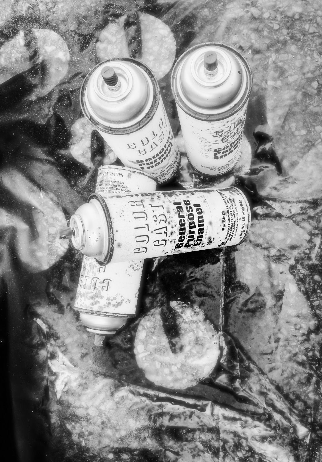 “Four old black spray paint cans used to repaint a repurposed garage sale sign project, sitting on a tarp outdoors.”
