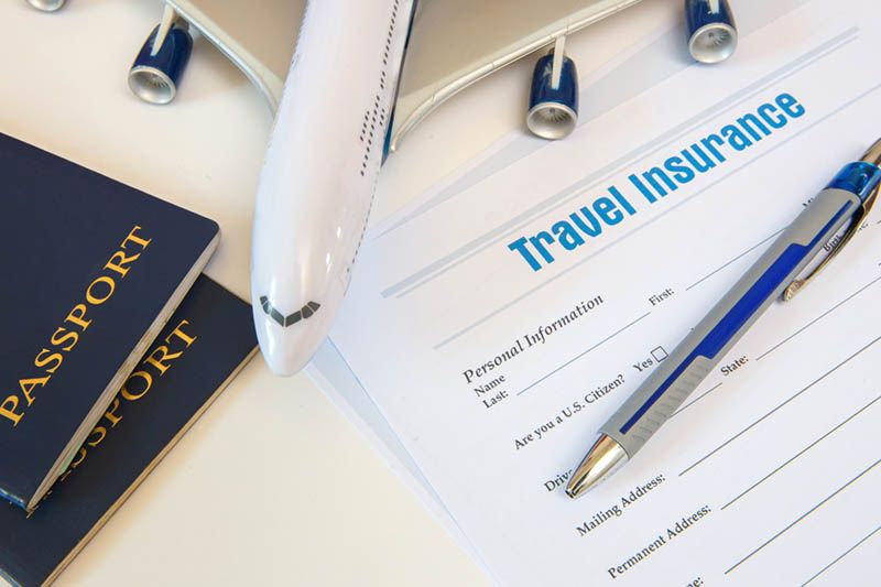Travel insurance form with passports, pen, and airplane model on desk