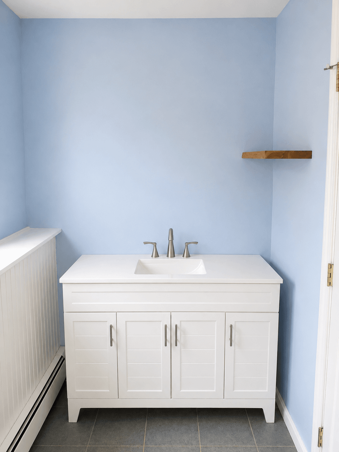White bathroom vanity beneath pale blue walls and a wood floating shelf