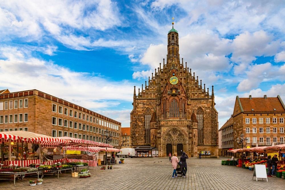 Historic church and market square in Nuremberg, Germany, with striped vendor stalls beneath a bright blue sky.
