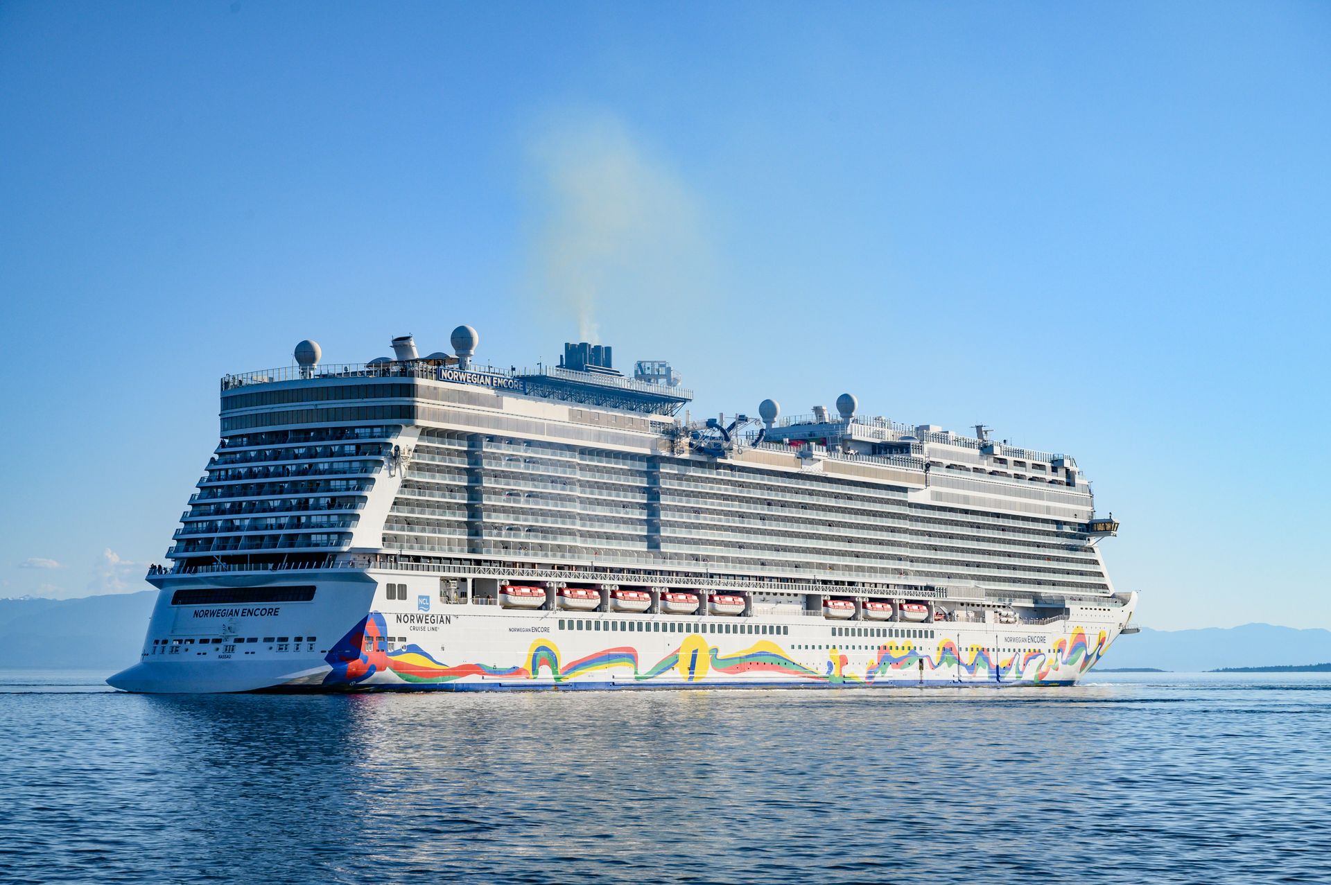 Norwegian Encore cruise ship sailing on calm blue water beneath a clear blue sky, offering a convenient way to experience an Alaska cruise.