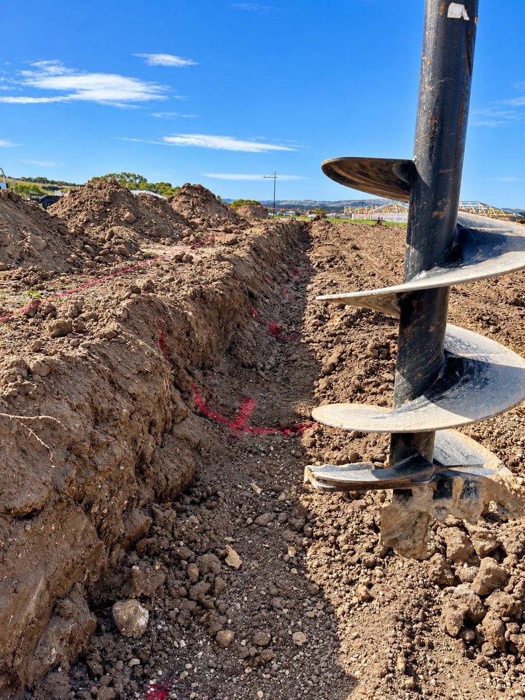 Auger preparing footing holes on a retaining wall site