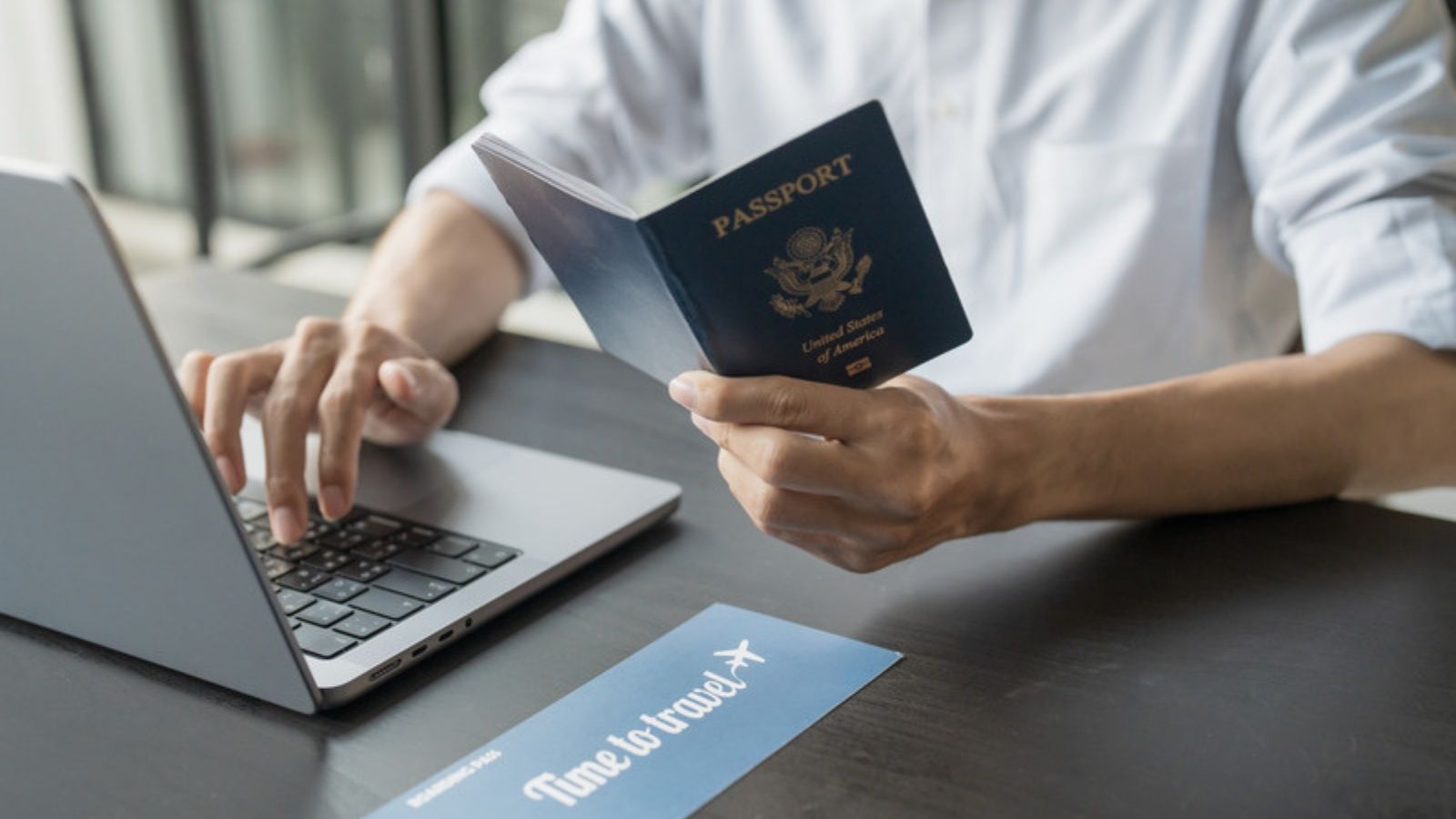 Traveller holding a passport while using a laptop, The VPN Myths I Keep Having to Correct Traveller holding a passport while using a laptop, The VPN Myths I Keep Having to Correct