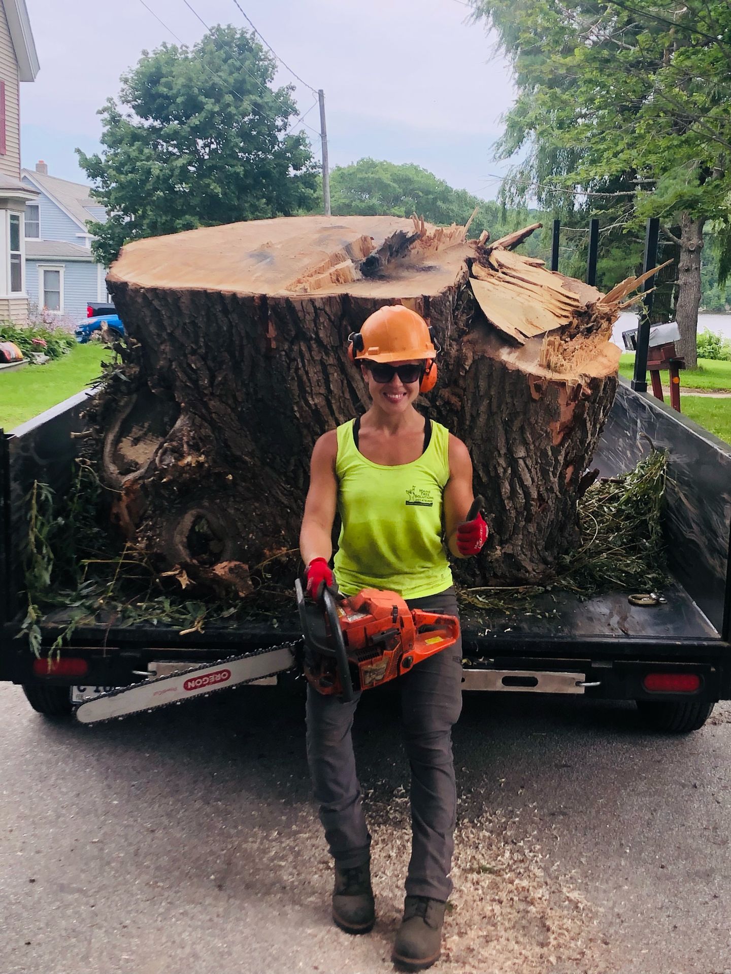 Female tree service professional from Well Rounded Tree Service in Central Maine holding a chainsaw in front of a large cut tree trunk, providing expert tree removal and land clearing services.