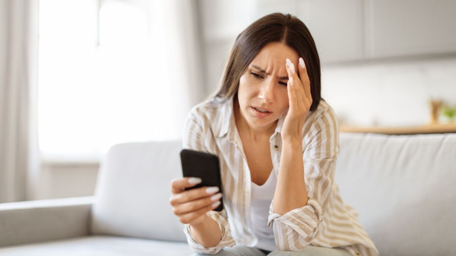 Worried woman looking at a suspicious message on her phone, Why Bad Grammar Doesn't Give Scam Messages Away