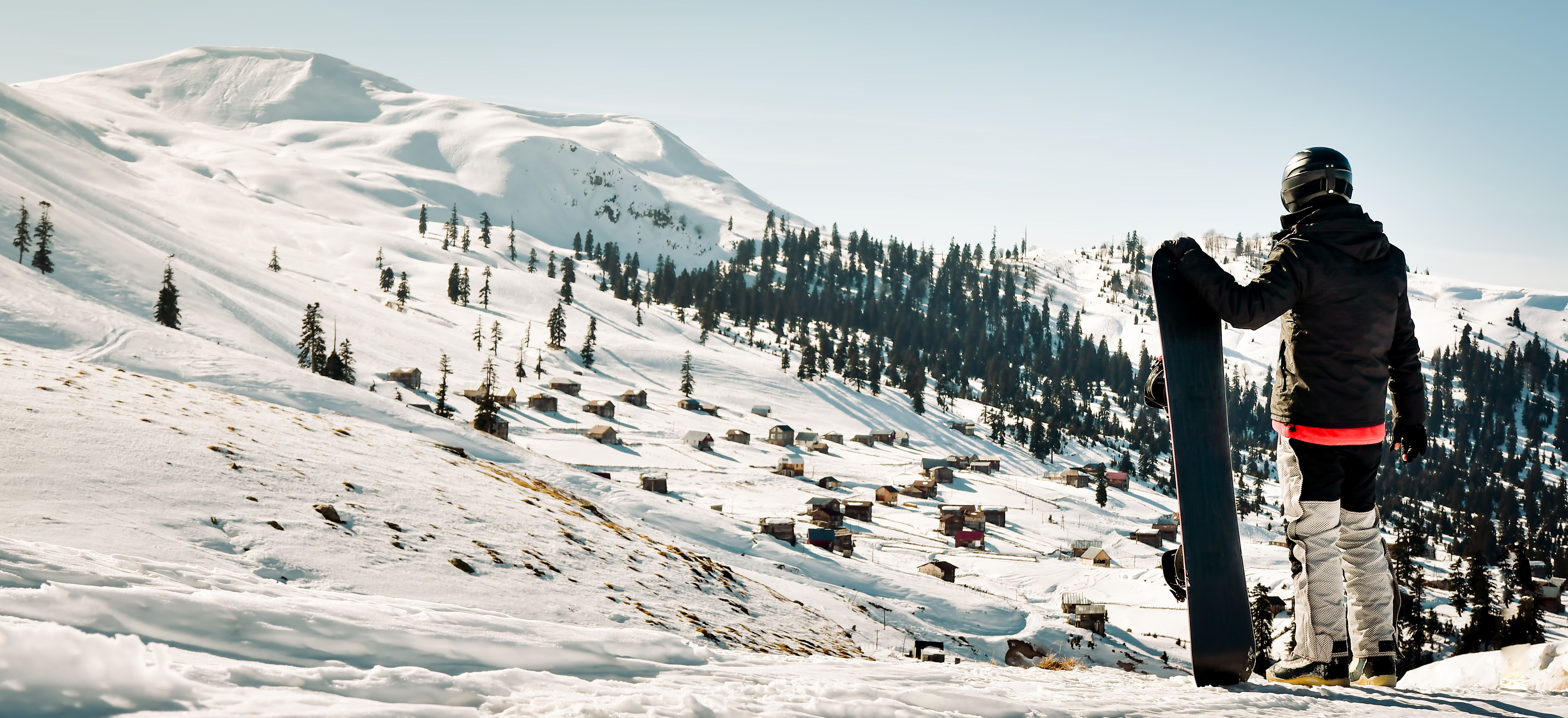 Male snowboarder dressed in dark black sportswear stand enjoy panorama of ski resort landscape on mountain slope in Georgia ski holiday destination - Goderdzi, Caucasus mountains