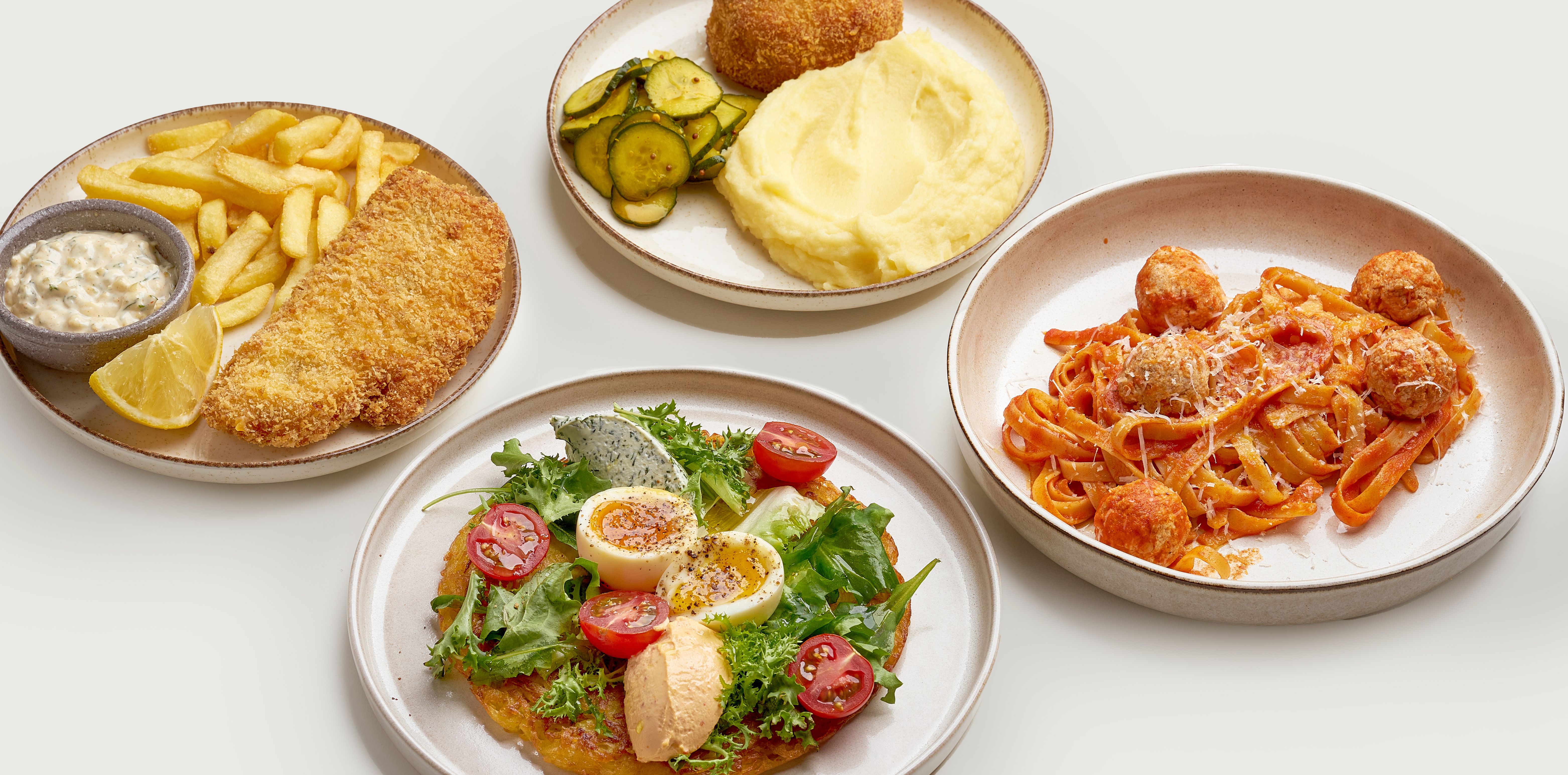 A variety of delicious and appetizing dishes are arranged on a white surface. The dishes include a bowl of creamy soup, a plate of meatballs and pasta, a plate of mashed potatoes A variety of delicious and appetizing dishes are arranged on a white surface. The dishes include a bowl of creamy soup, a plate of meatballs and pasta, a plate of mashed potatoes