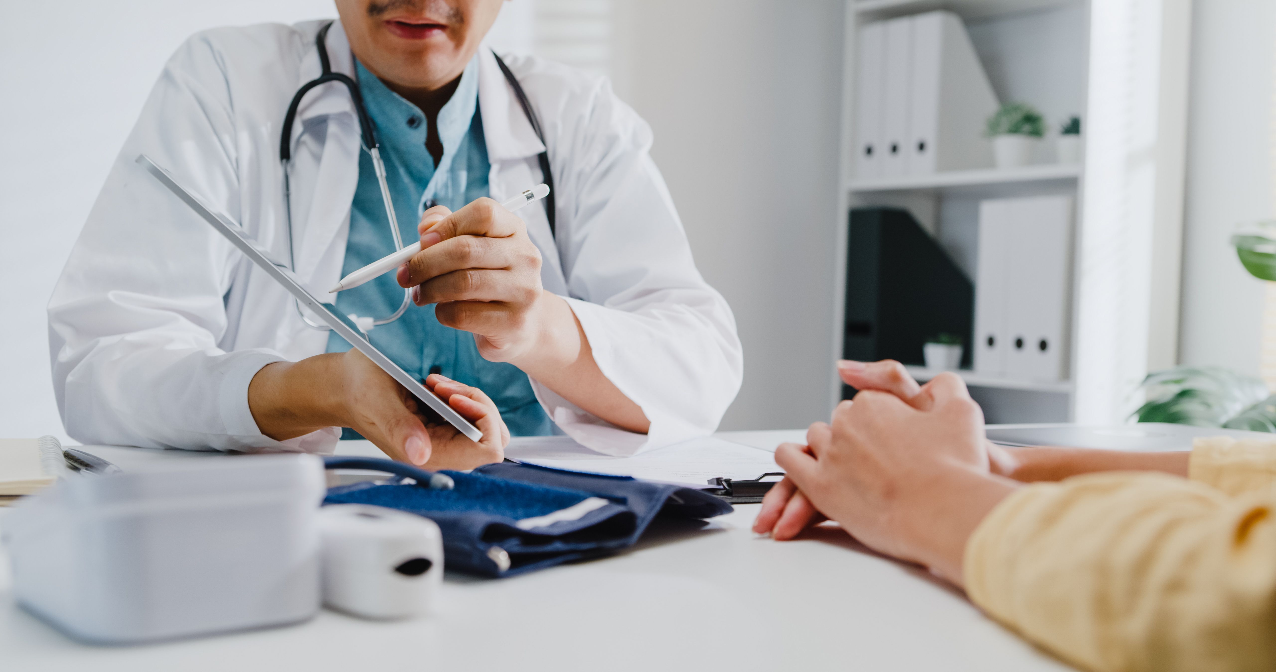 Close up of mature Asian man doctors medical results during consultation on tablet computer with woman patient in health clinic.