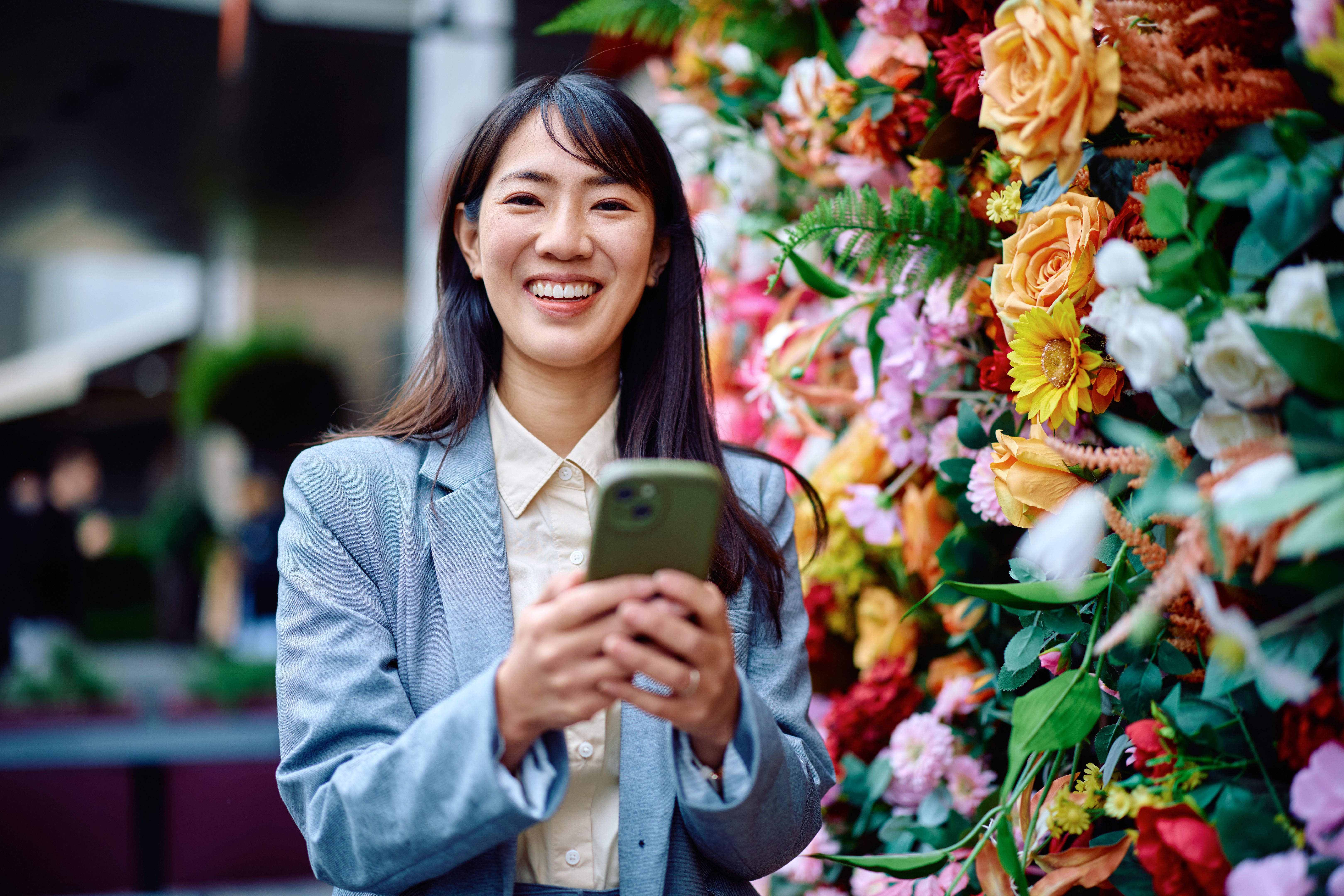 Young businesswoman smiling and using smartphone in front of flower wall