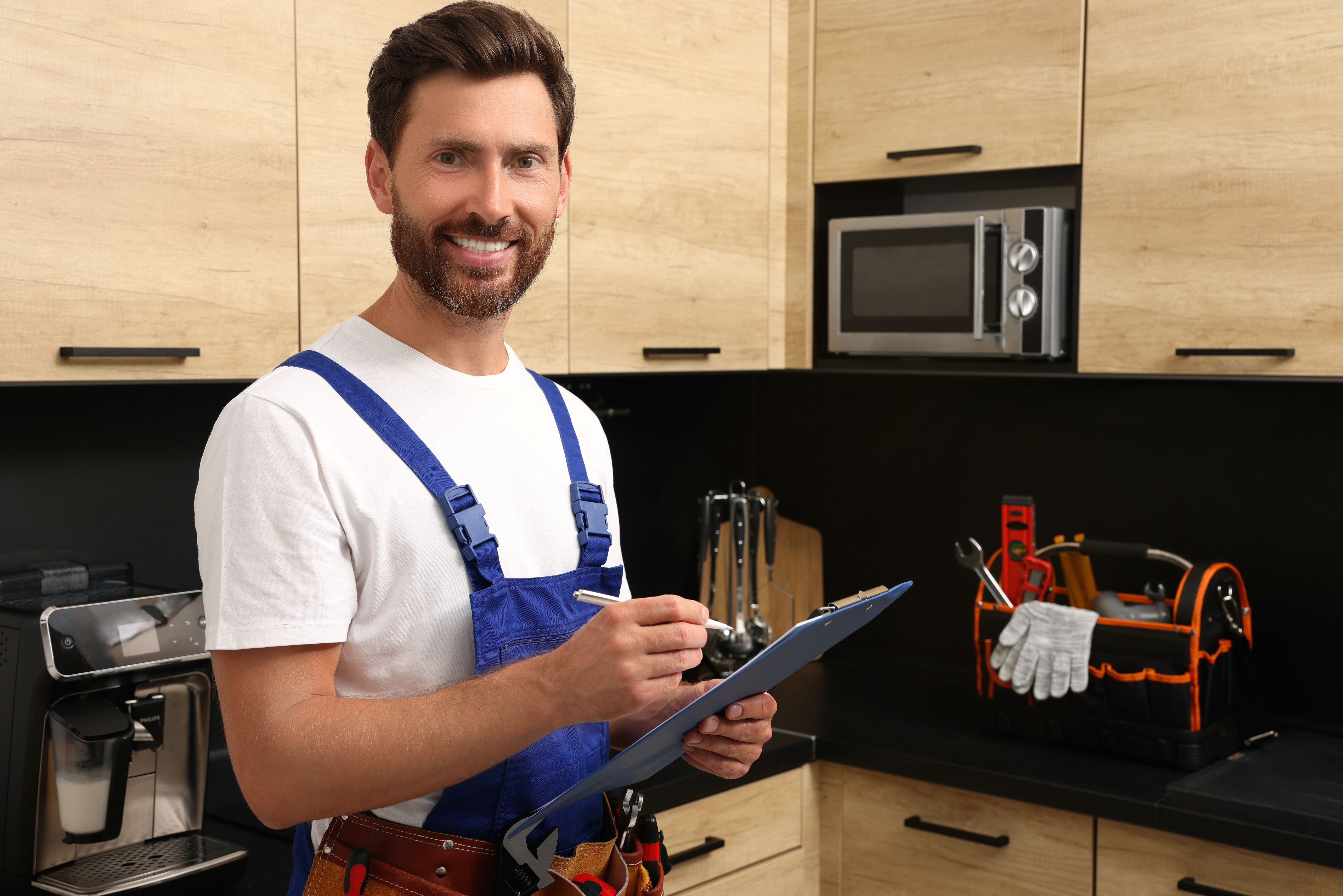 Professional plumber with clipboard and tool belt in kitchen Professional plumber with clipboard and tool belt in kitchen