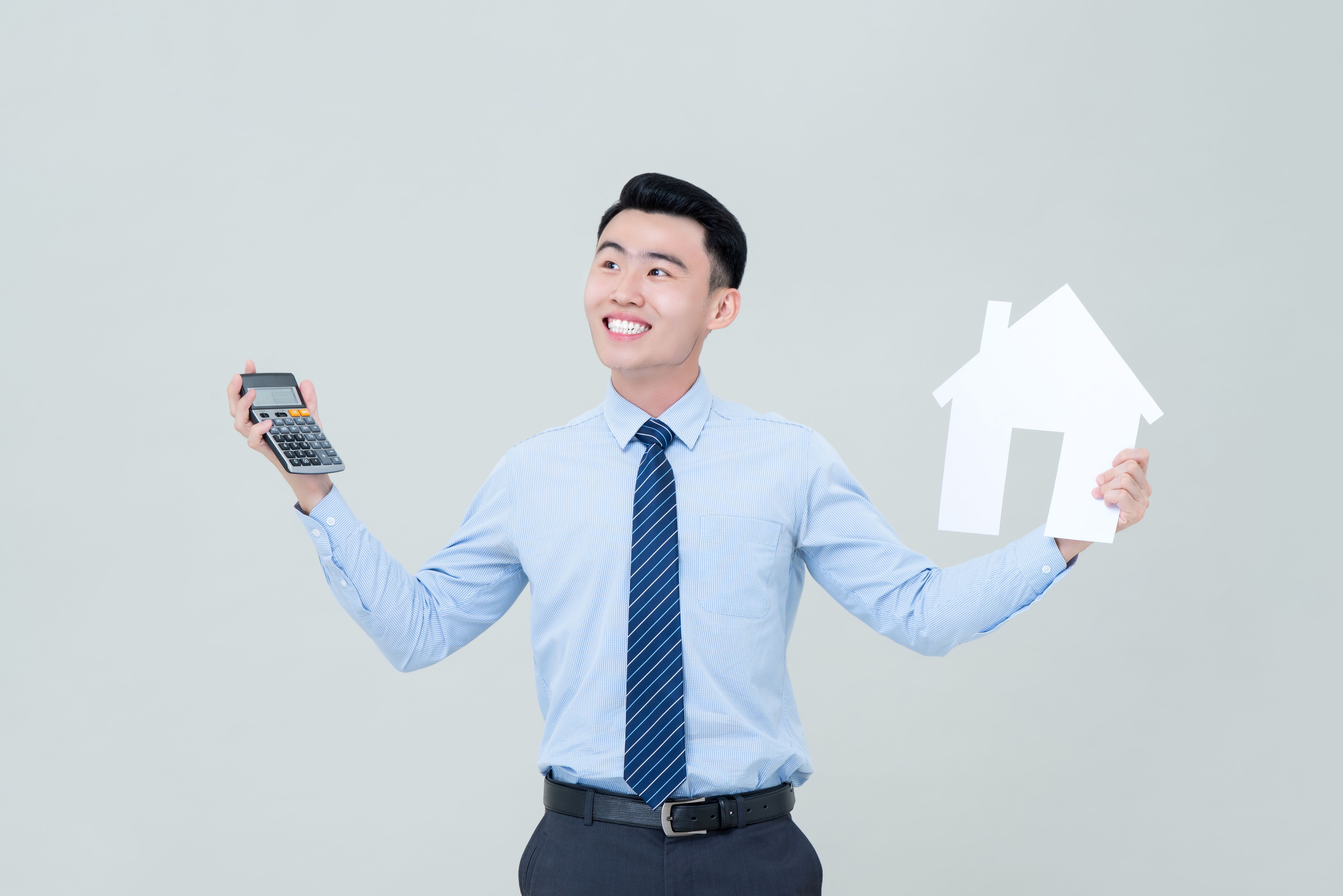 Young smiling Asian male real estate agent holding calculator and house cutout