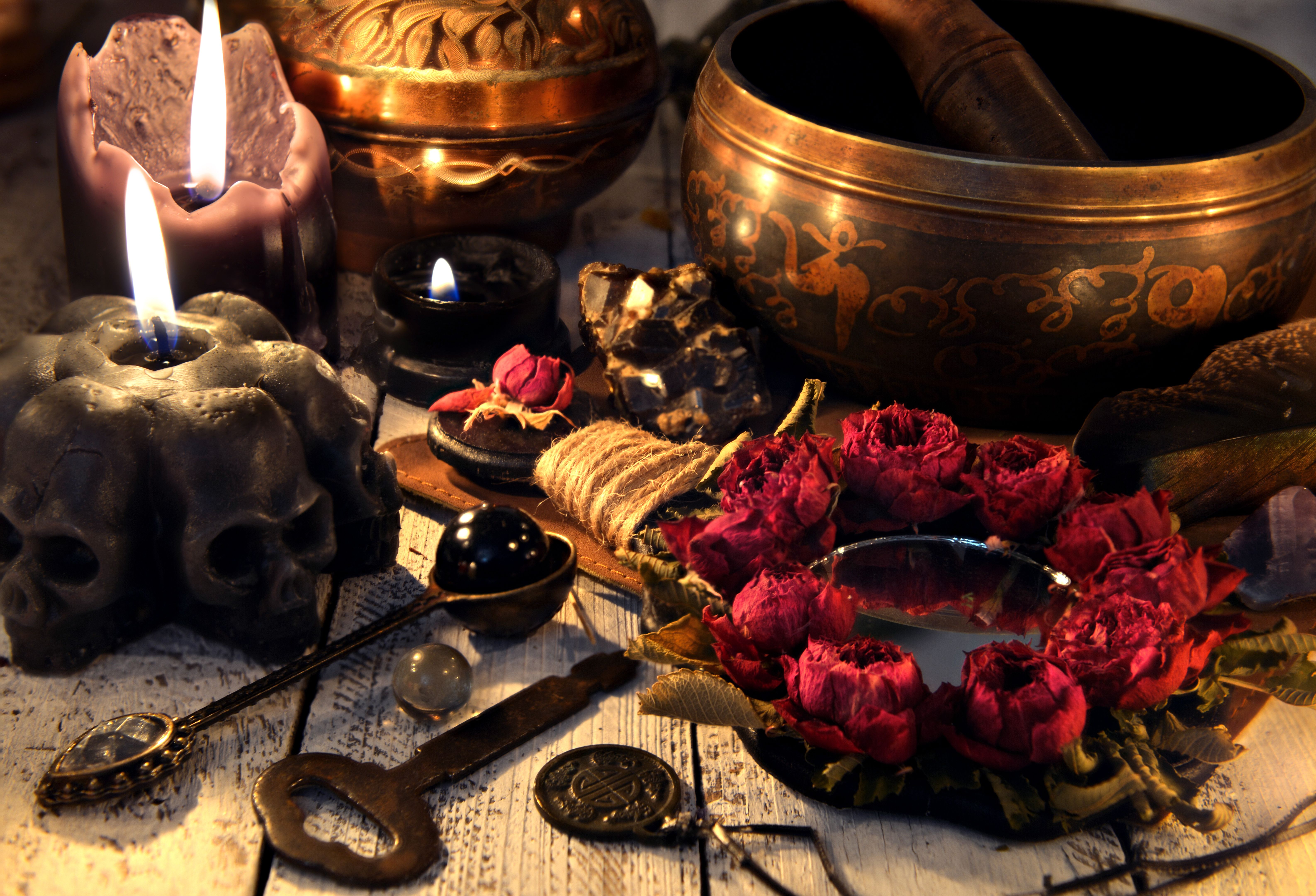 Black candles with skulls, rose mirror, metal key and singing bowl on witch table.