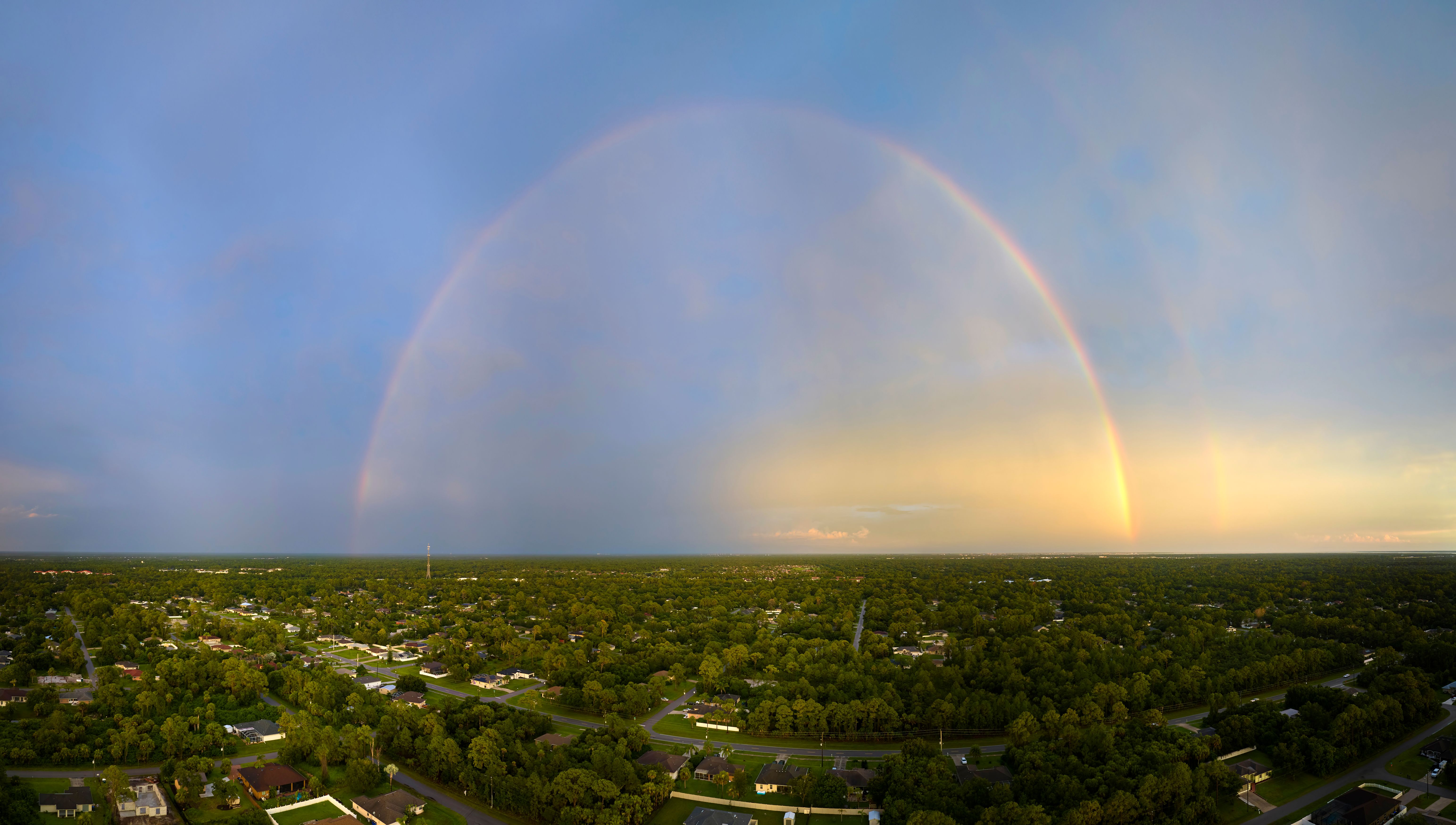 Colorful round rainbow over rural town suburbs against blue evening sky after heavy thunderstorm