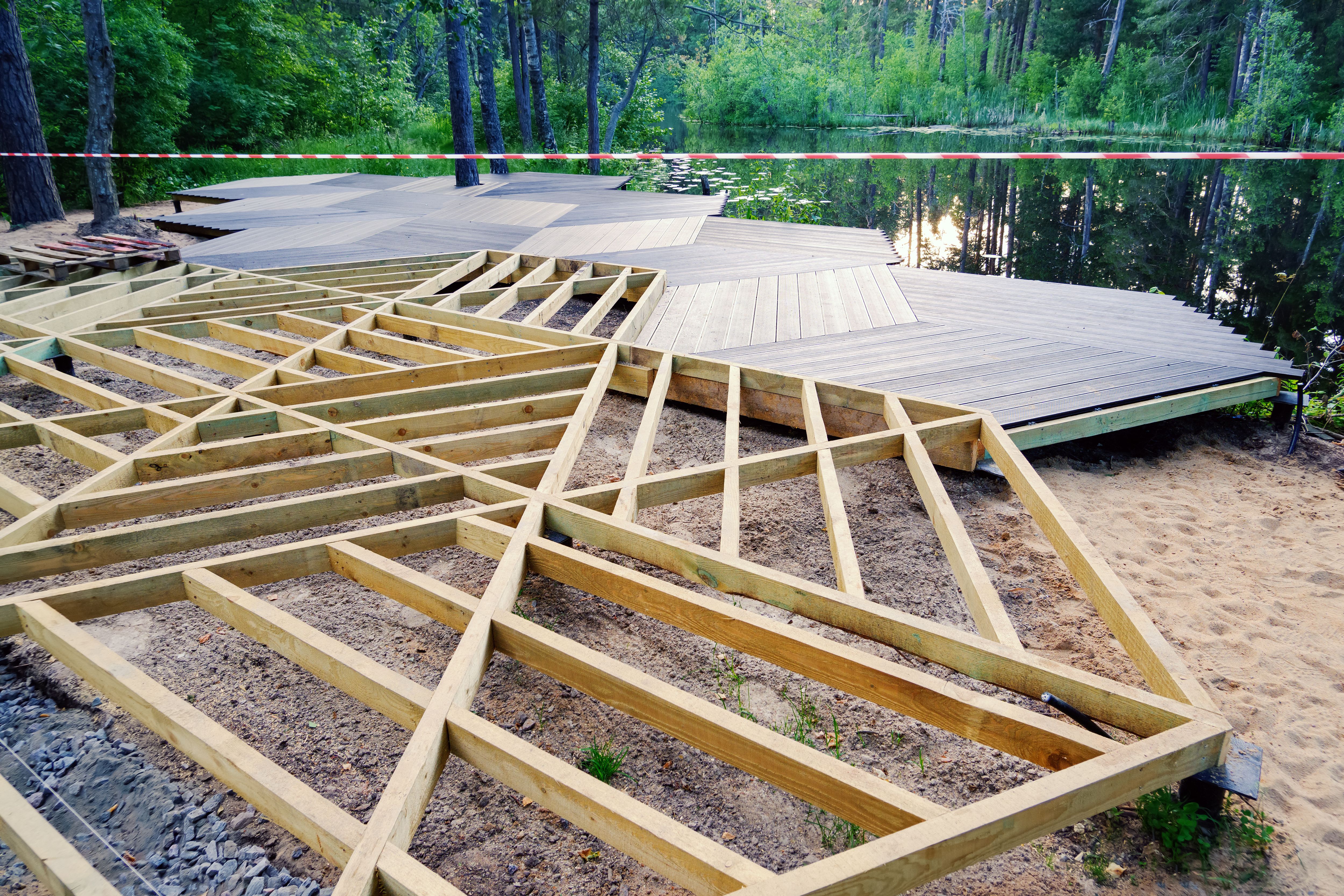Walking area on screw piles, wooden frame, plastic terrace board on pond shore in park, construction site