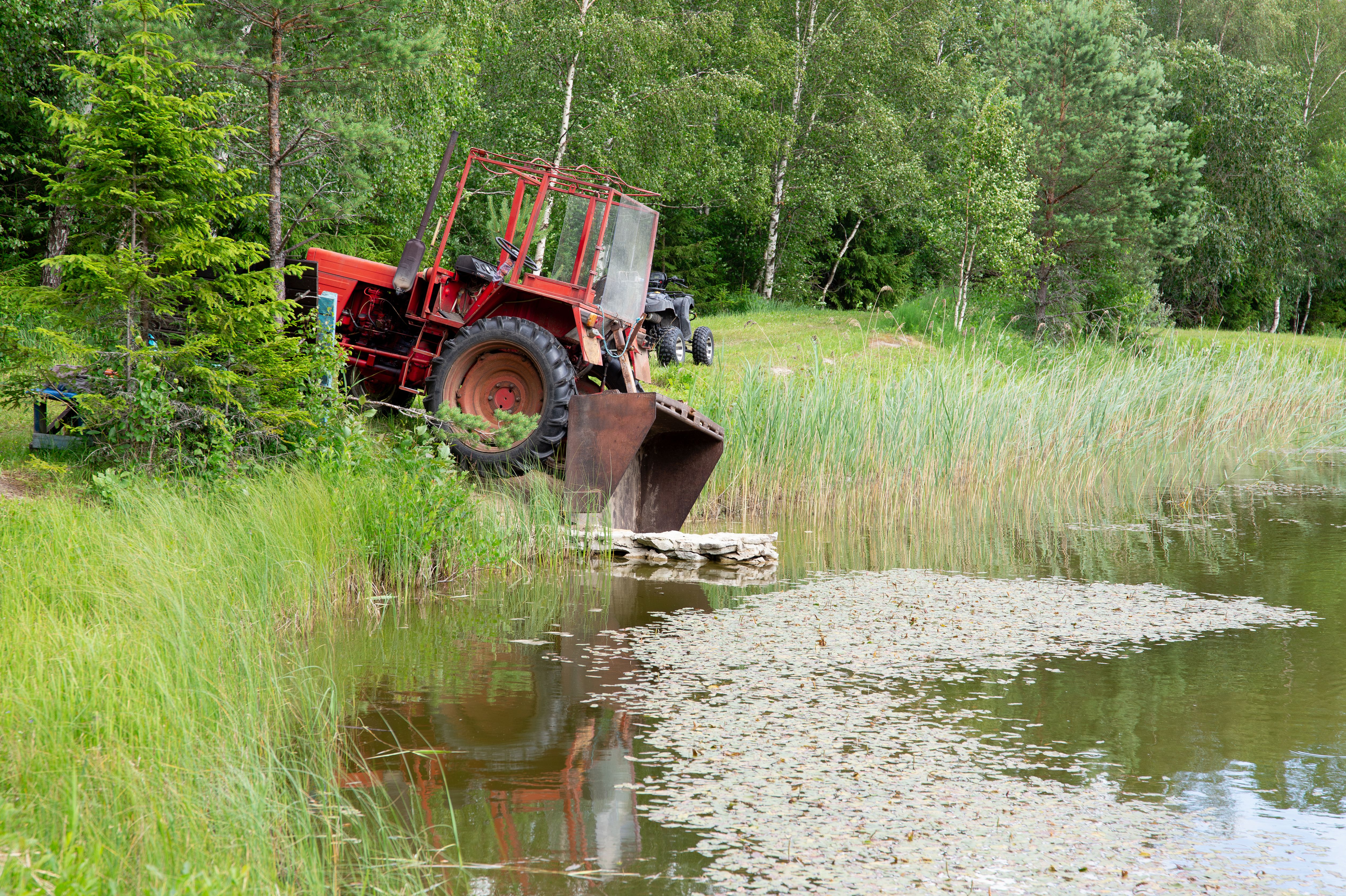 Old tractor in danger of falling and slipping in lake and overturn. Outdoors in summer.