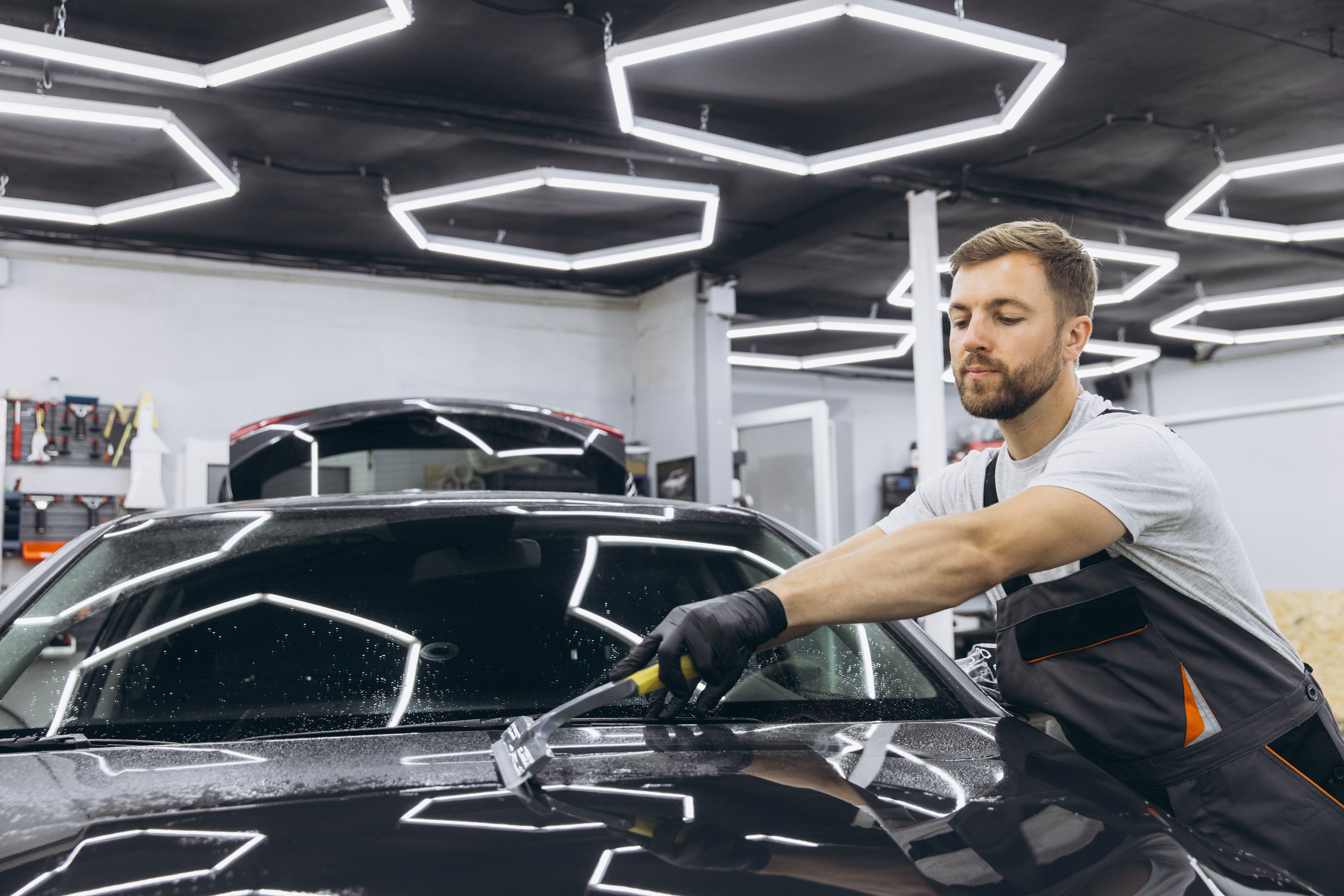 Man washing car hood and preparing the polishing process Car glass coating. Male worker installing protection film to car in garage. Car Detailing.