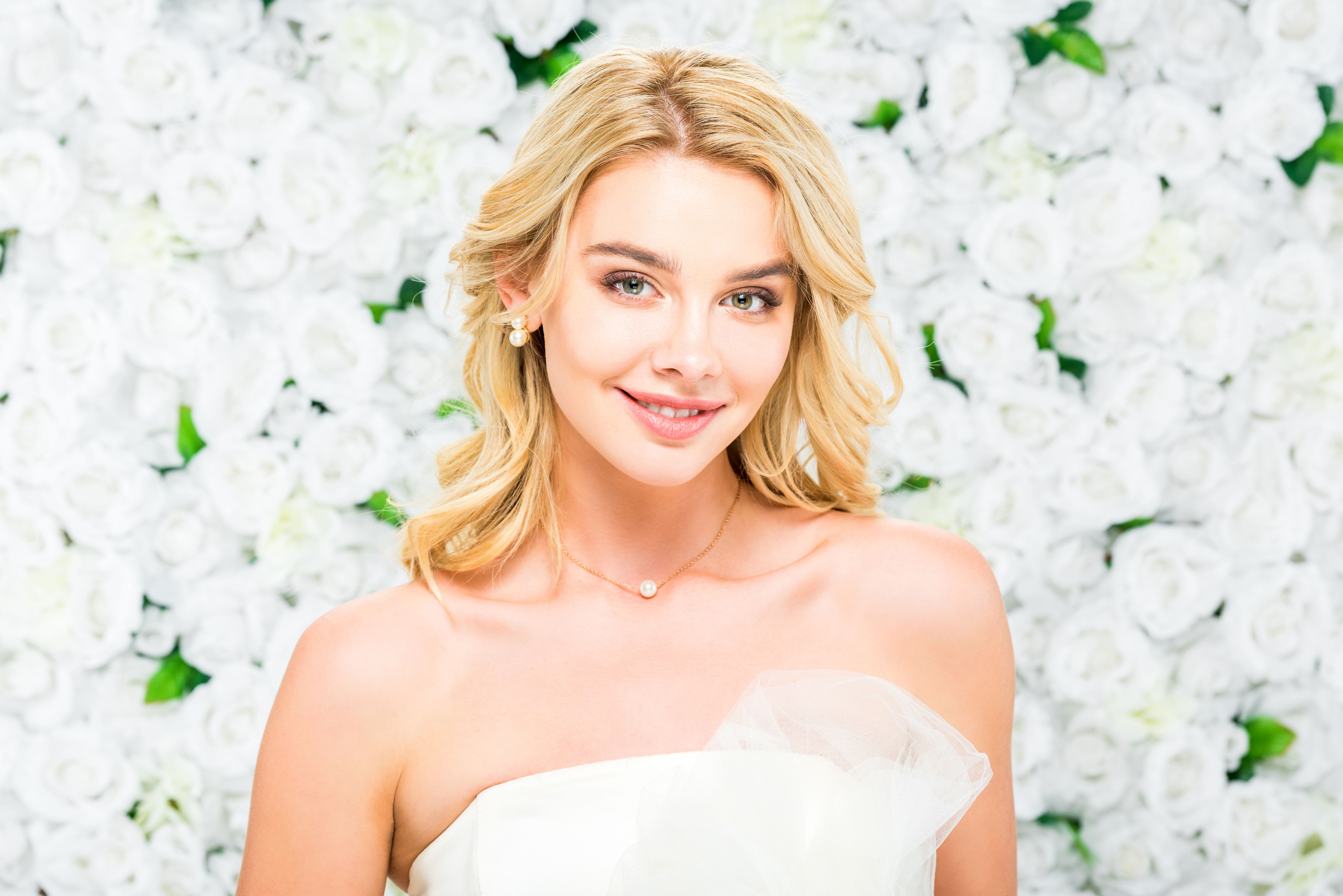 smiling pretty young woman with blonde hair looking at camera on white floral background