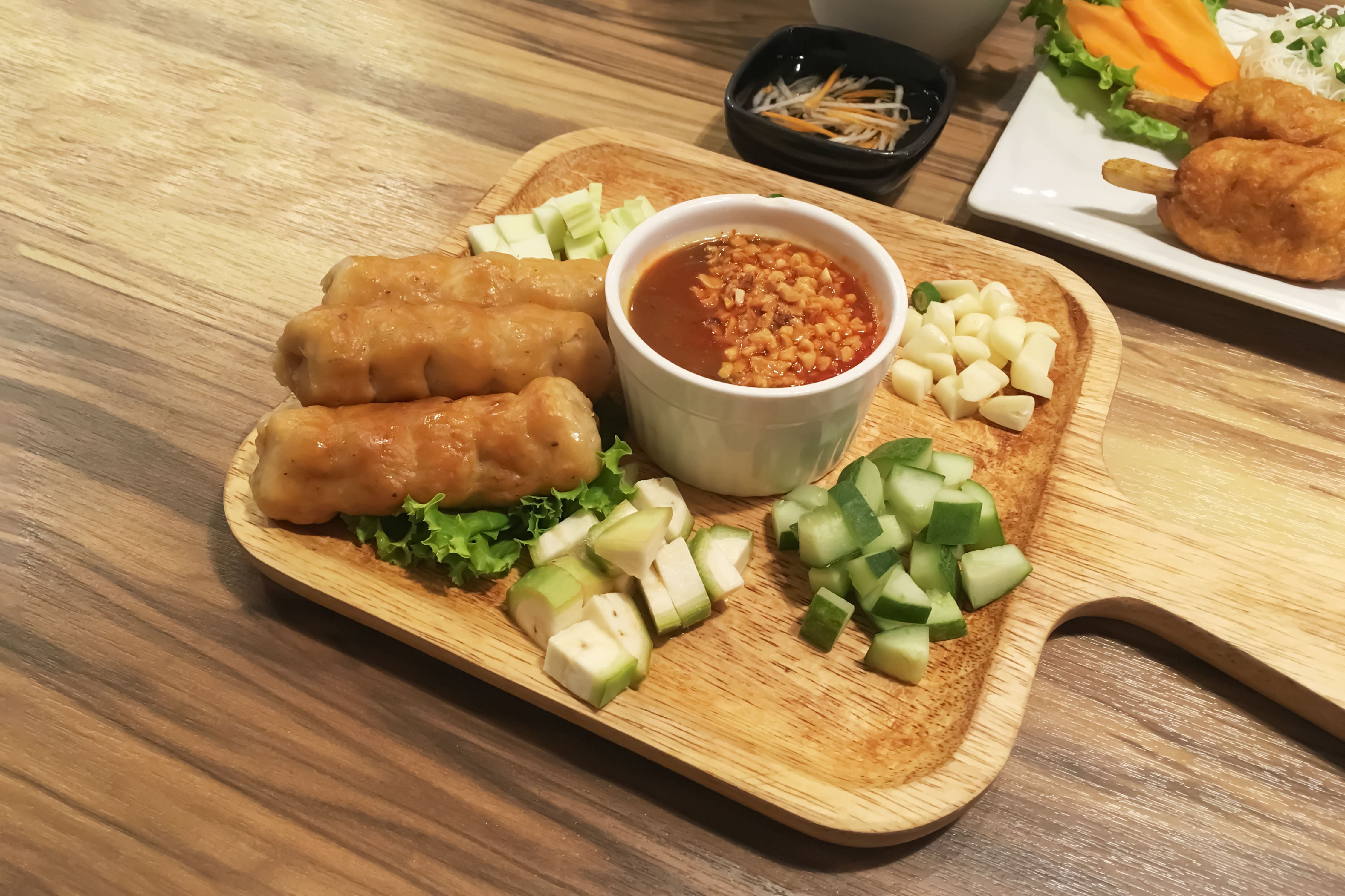 Vietnamese food name Nam Nueng wih grilled pork ball and mixed fresh vegetables and herbs with sweet and sour source in square wooden plate on wooden table.