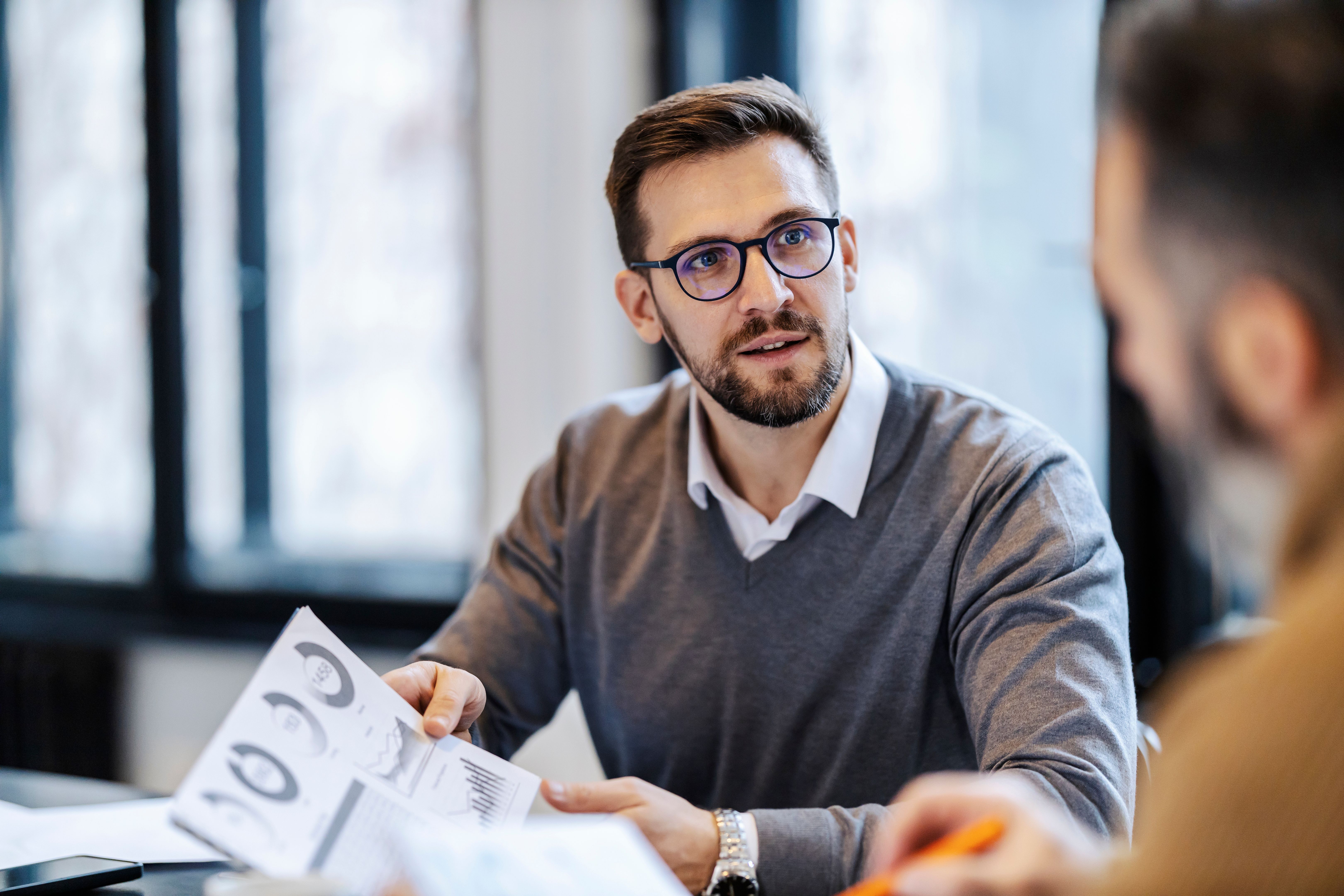 A businessman is holding document with charts and statistics and discussing with colleague on a business meeting in boardroom.