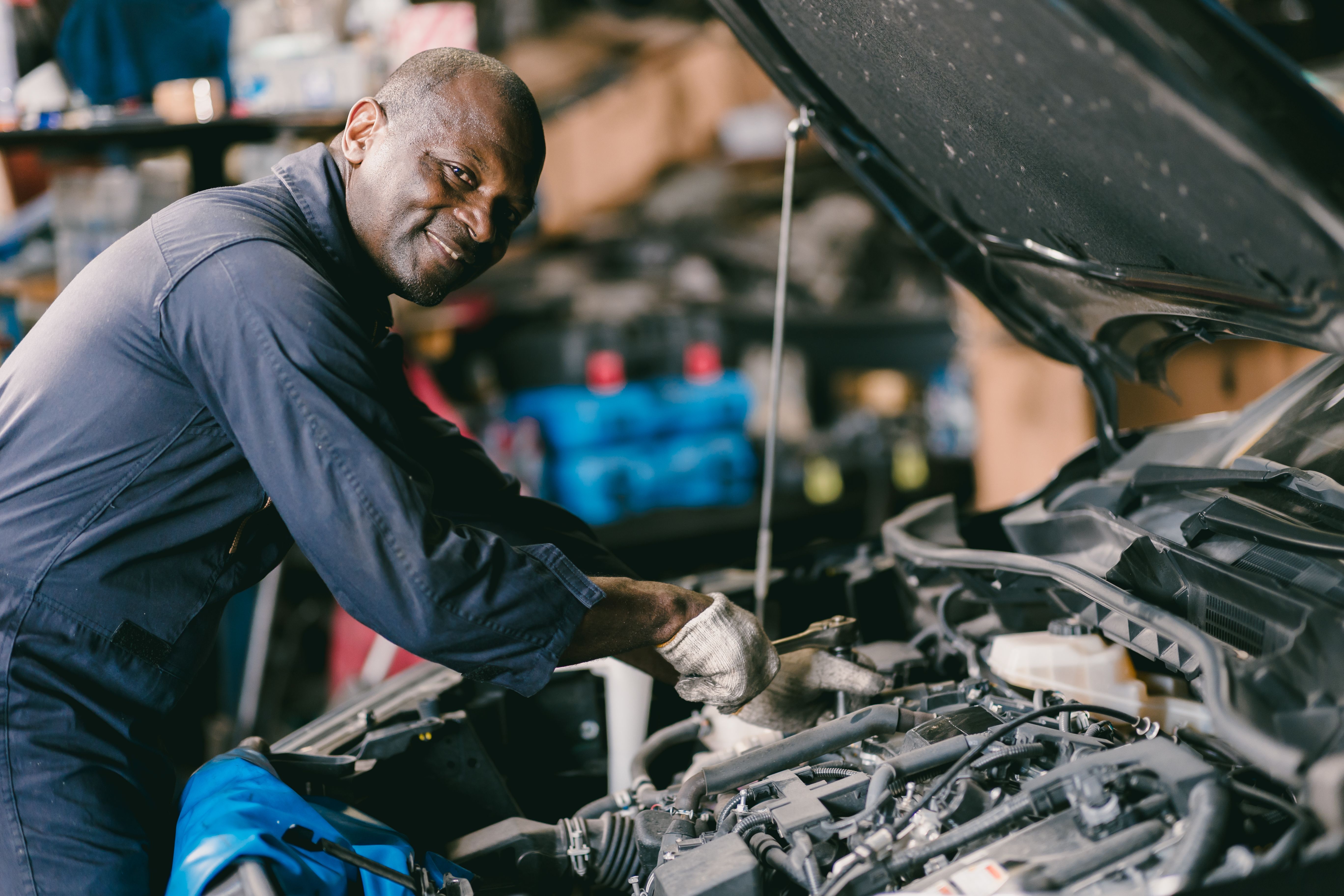 happy smiling mechanic male car engine service underhood checking oil replace in broken part at auto garage