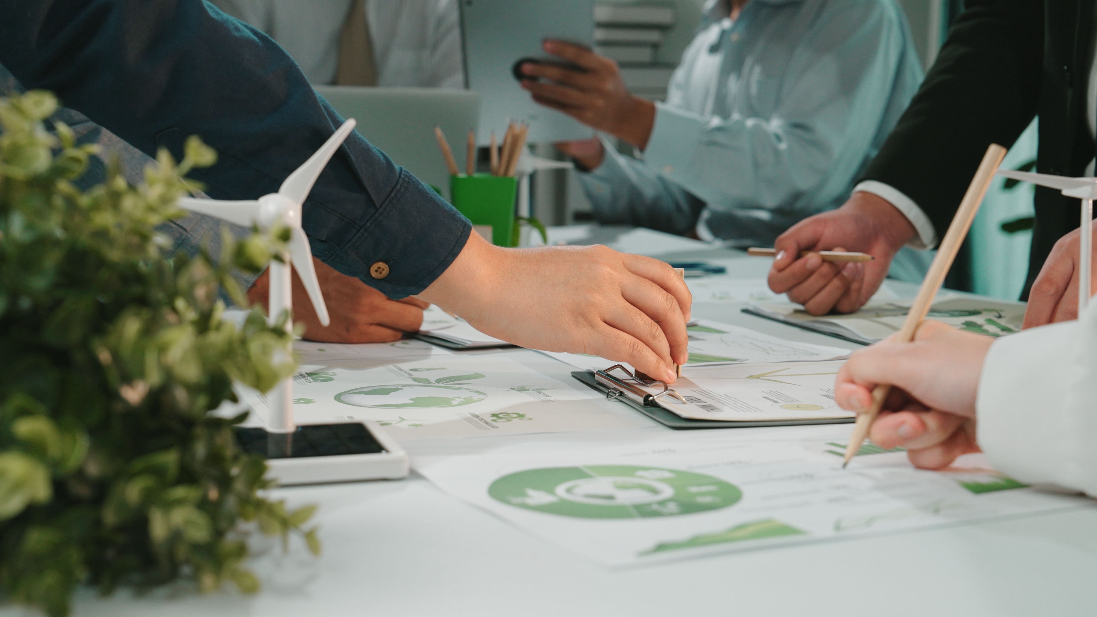 Collaborative Team Meeting on Sustainable Business Strategies with Charts, Graphs, and Wind Turbine Model in Modern Office Environment SACTR