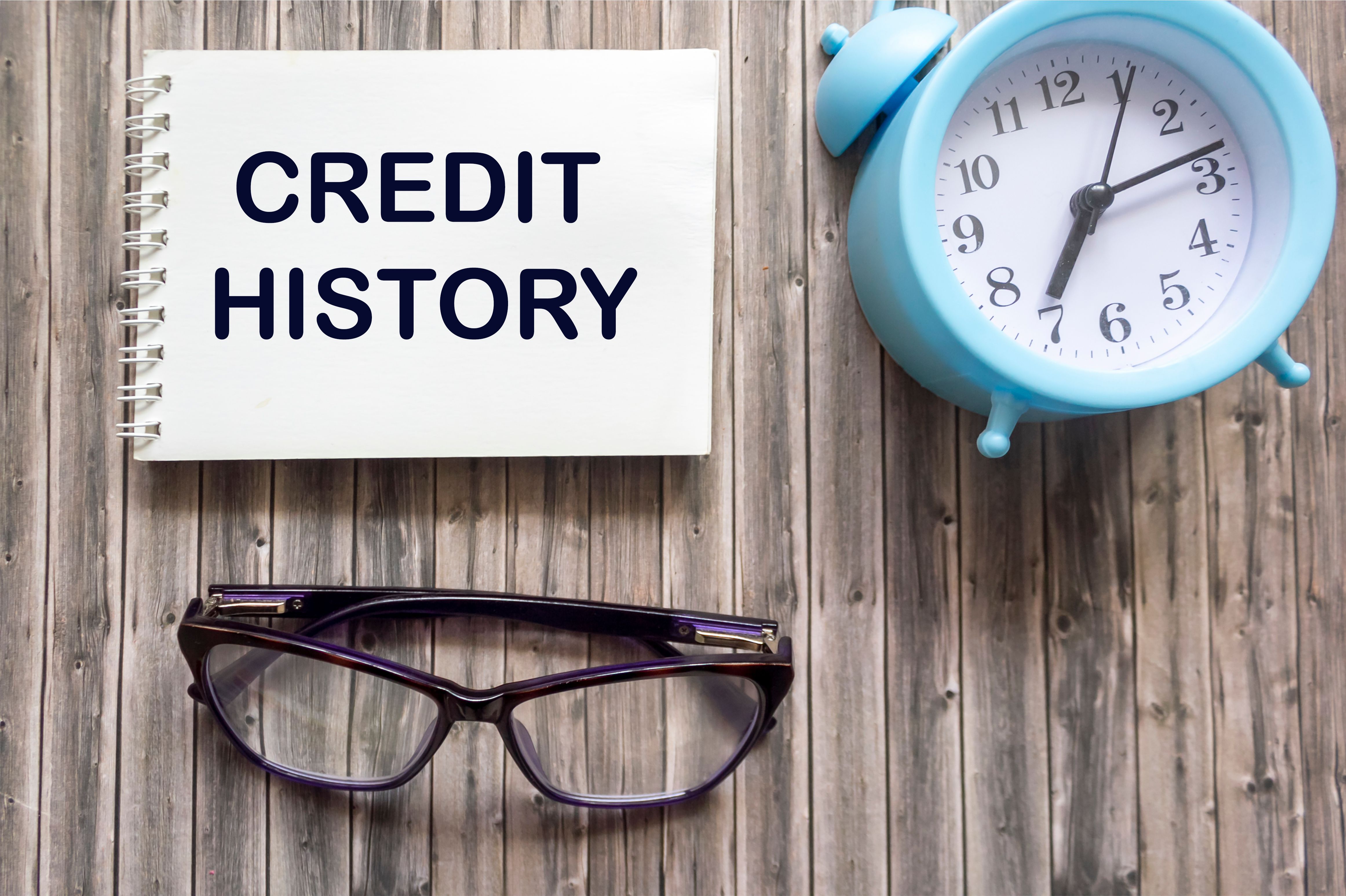 Credit history. text on notepad on wooden background with clock and glasses